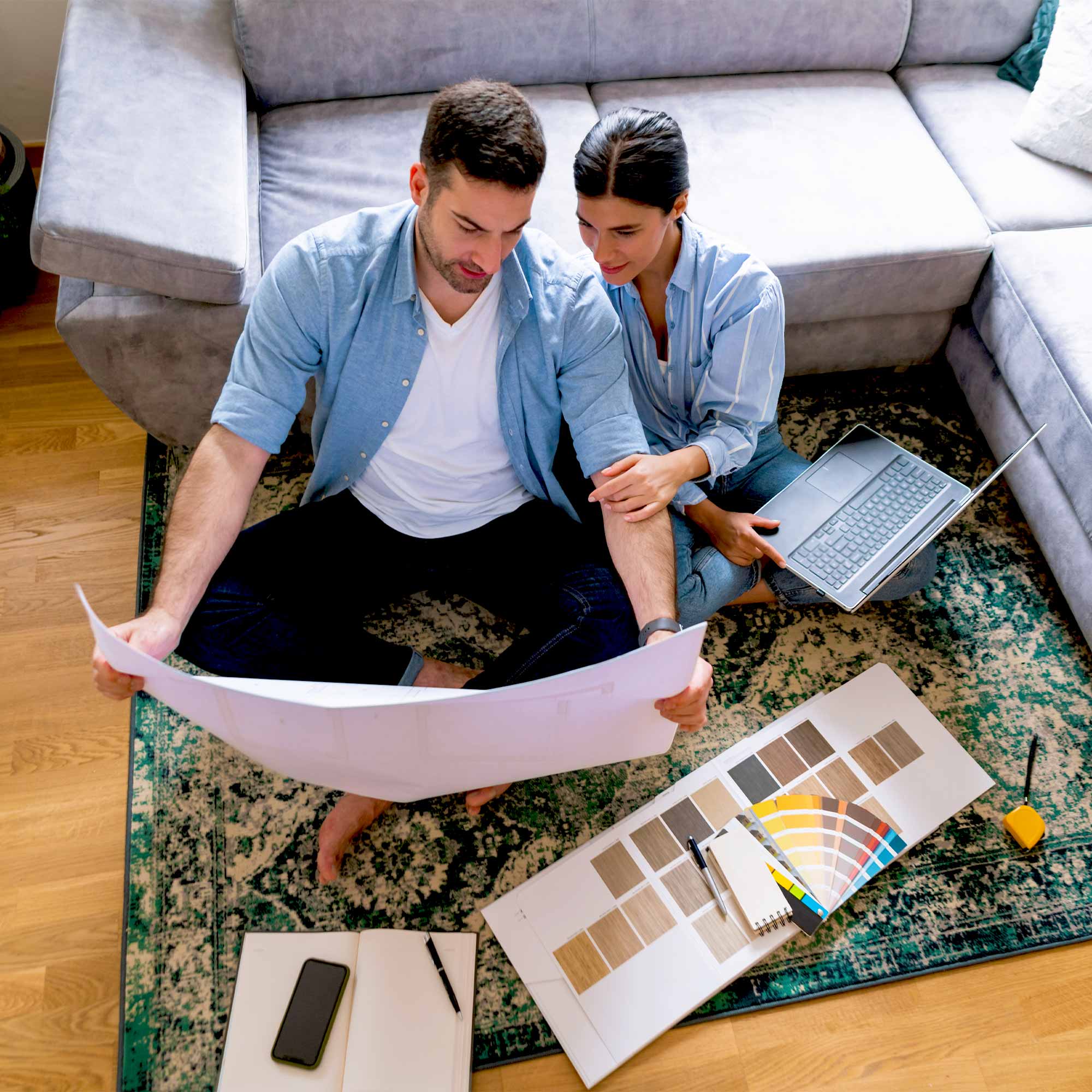 A man and a woman planning a home remodel as they sit on the living room floor.