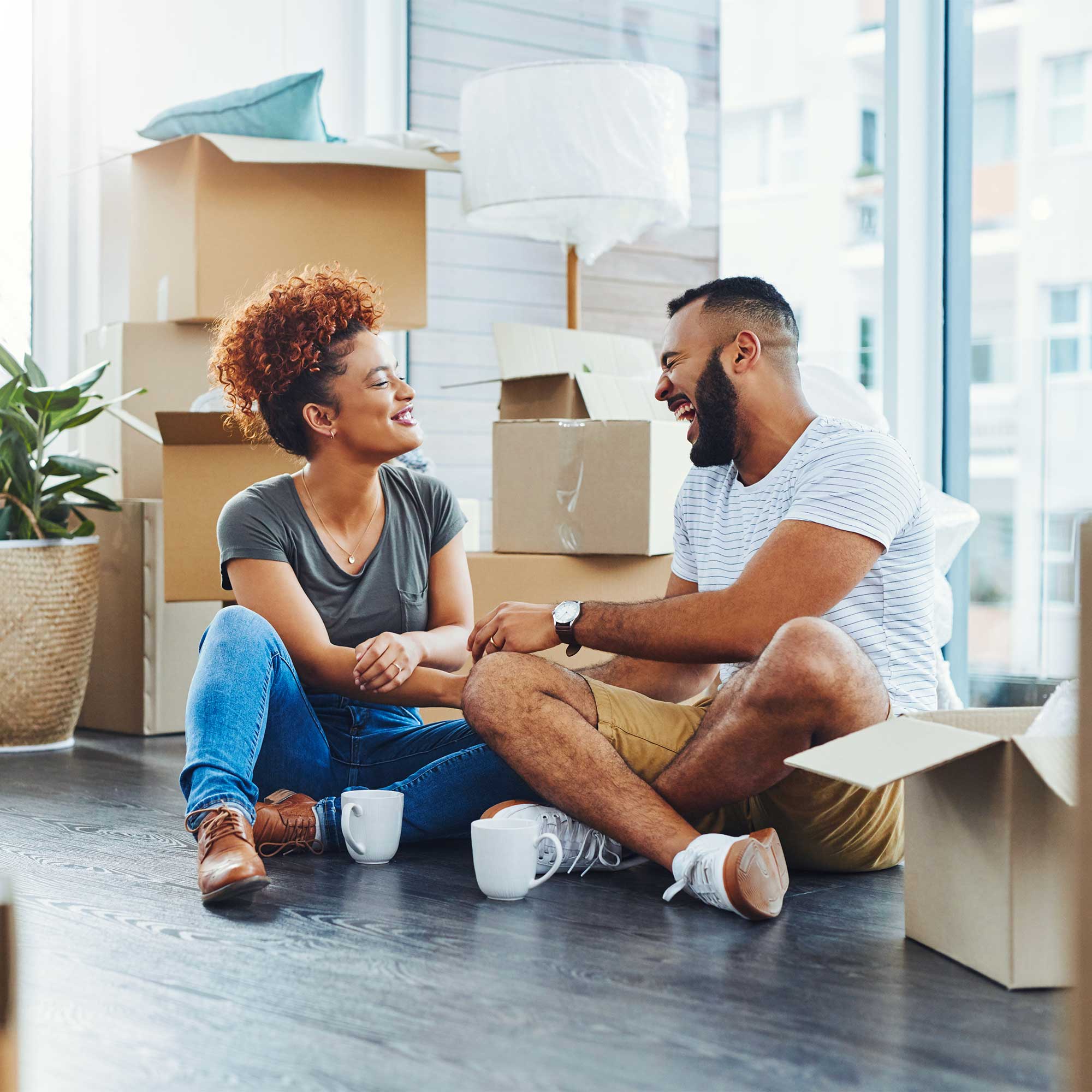 A man and a woman sit on the floor next to a pile of cardboard boxes.