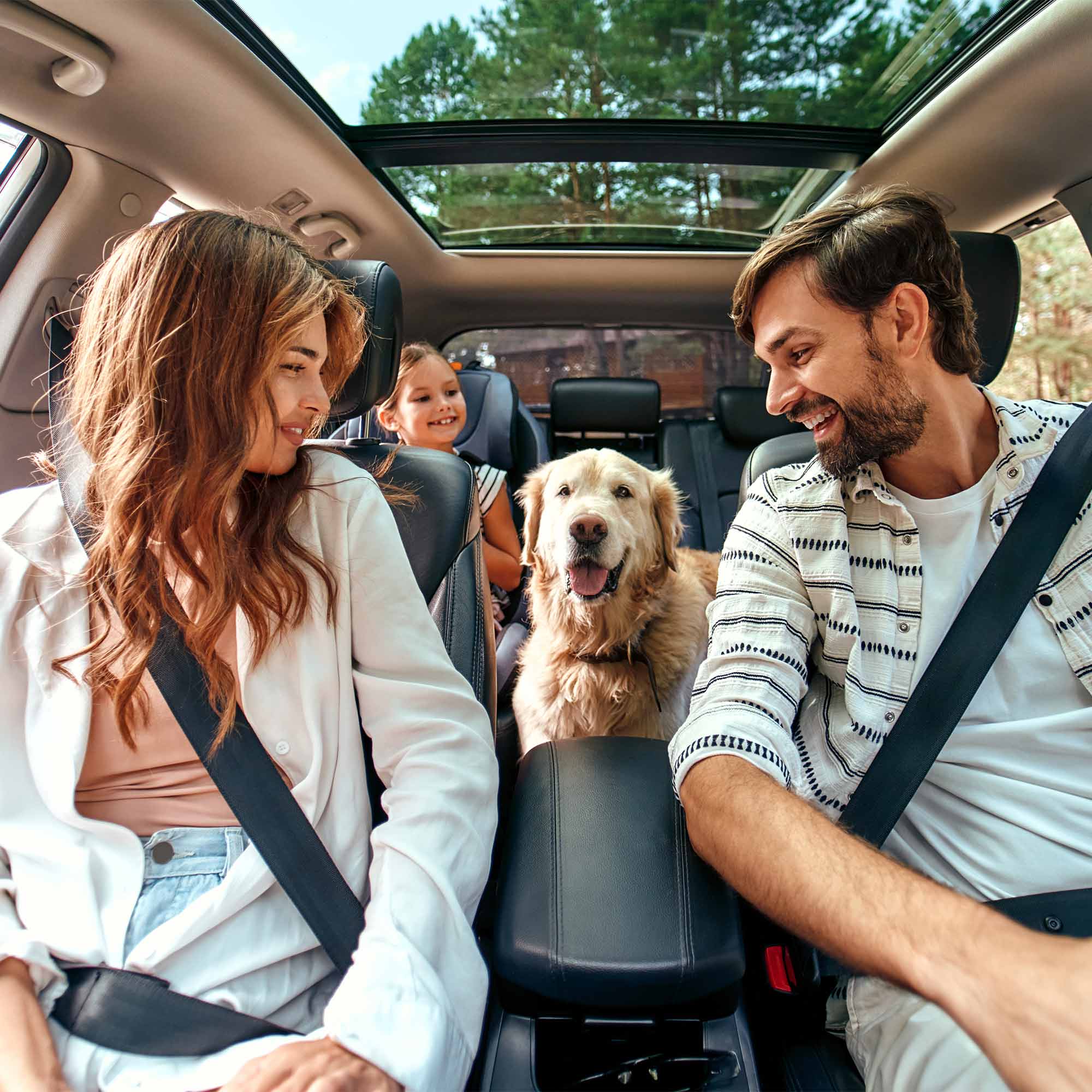 Couple loading up their daughter, luggage, and dog in the back of the car.
