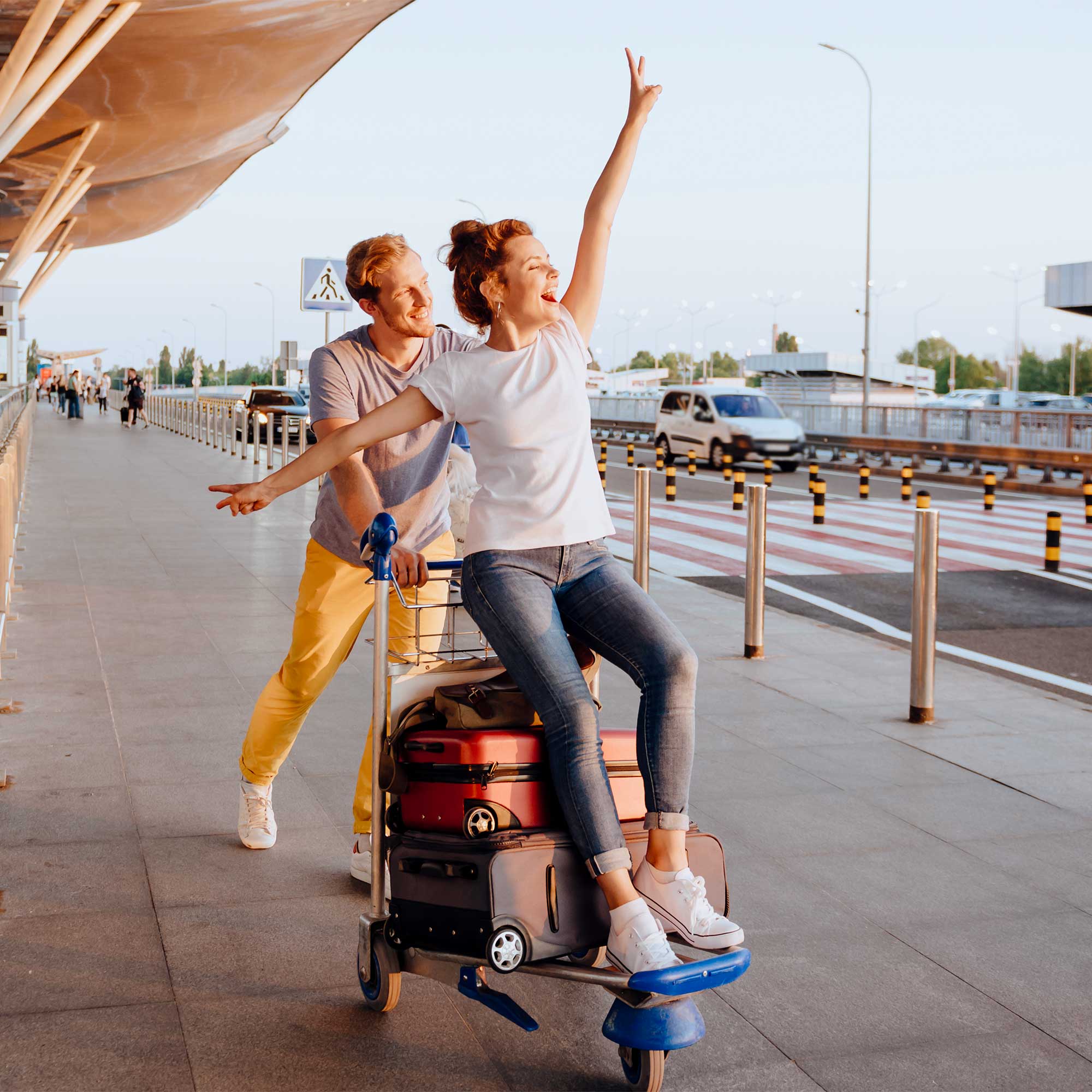 A lady rides the luggage cart as her husband pushes it.