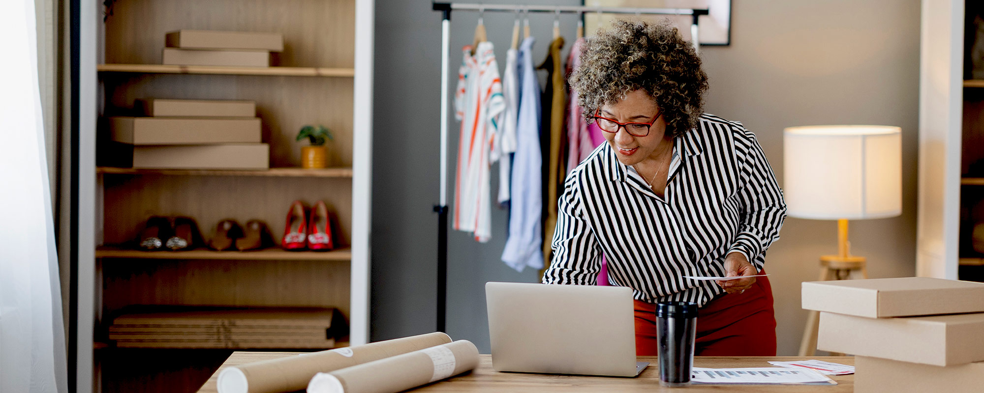 Woman wearing a white shirt and glasses peers at her computer screen with a mug in her hand.