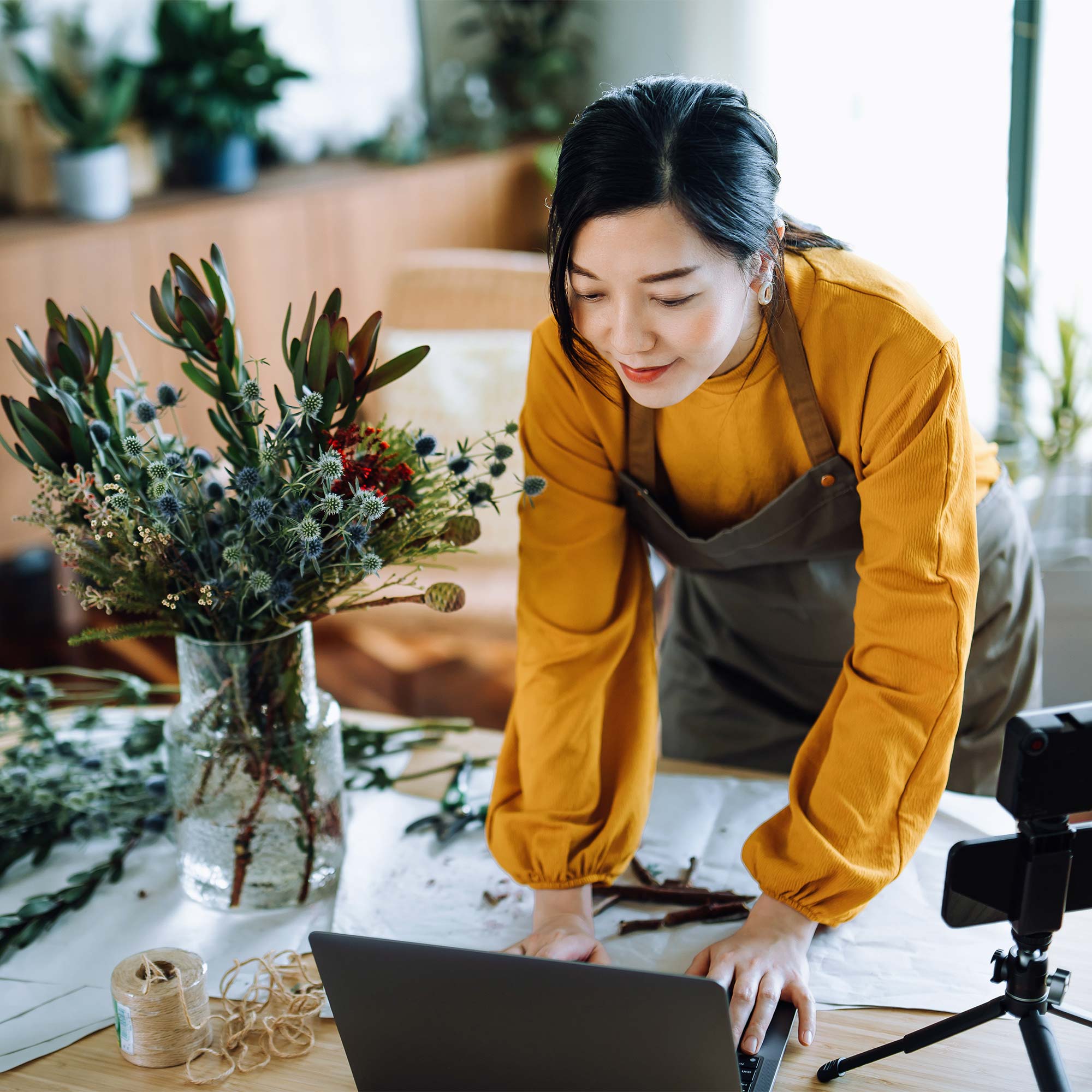 A man in a denim shirt holds his cell phone as he leans over to view the computer screen.