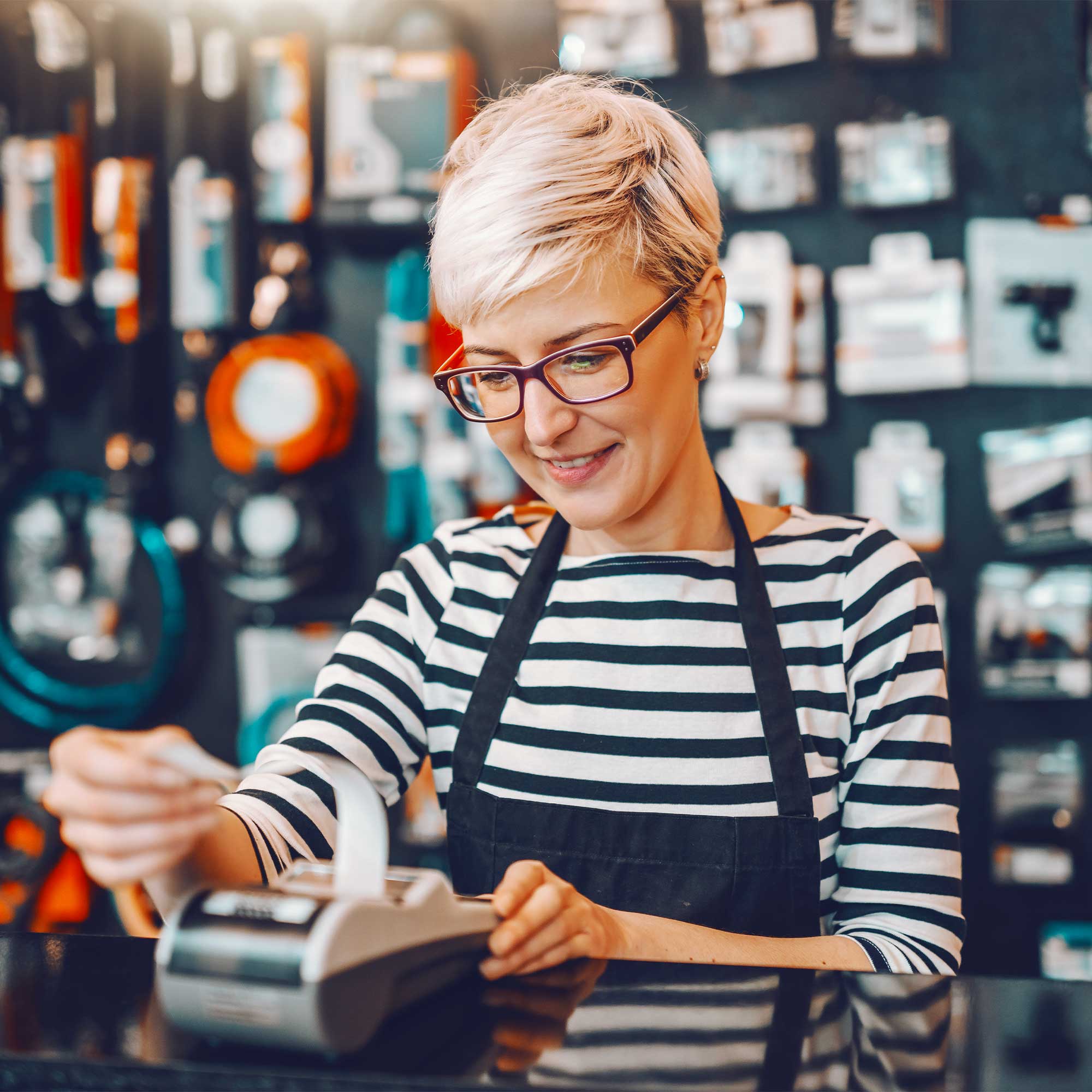Woman in striped shirt and apron prints a receipt and smiles.