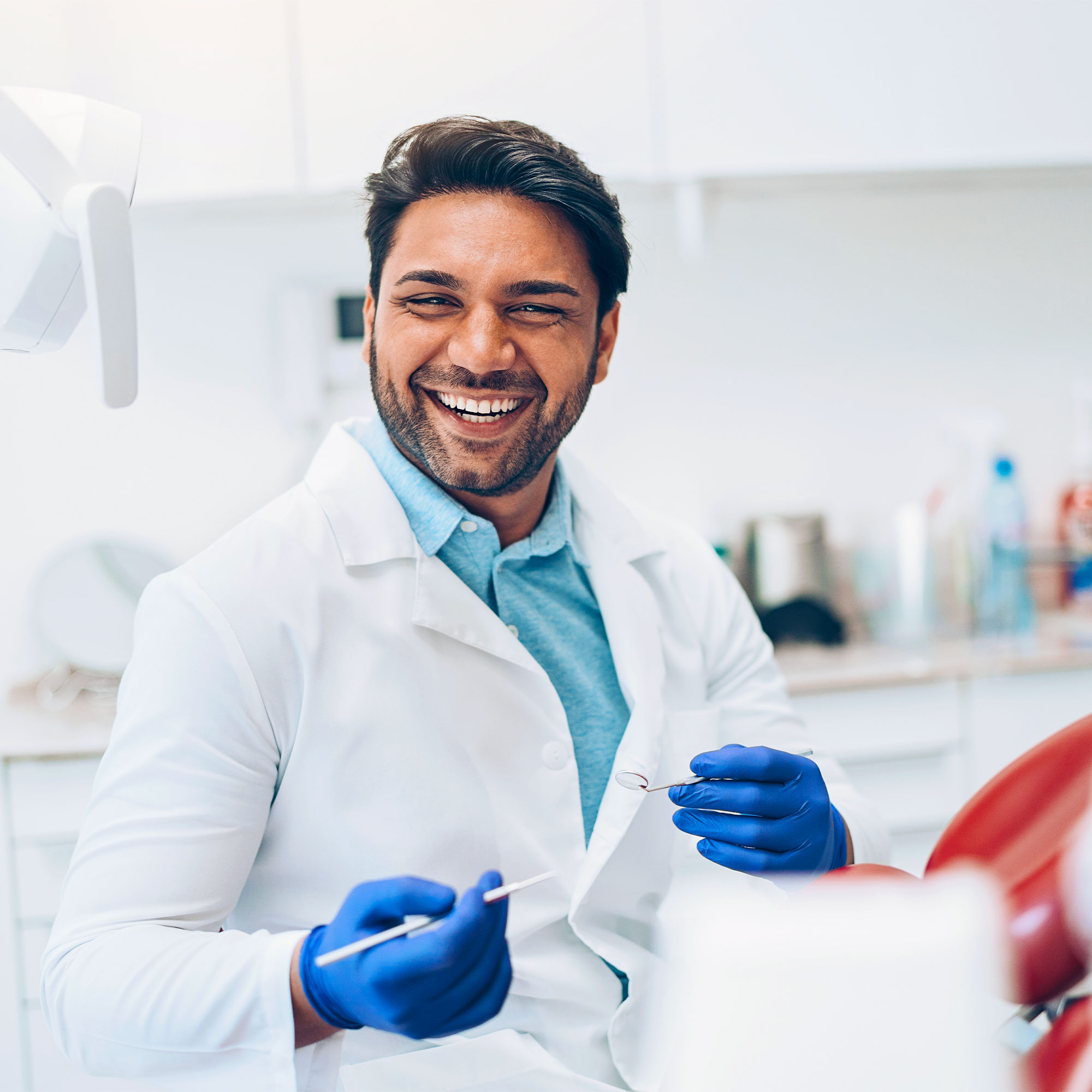 A doctor wearing blue gloves and white lab coat smiles in his office.