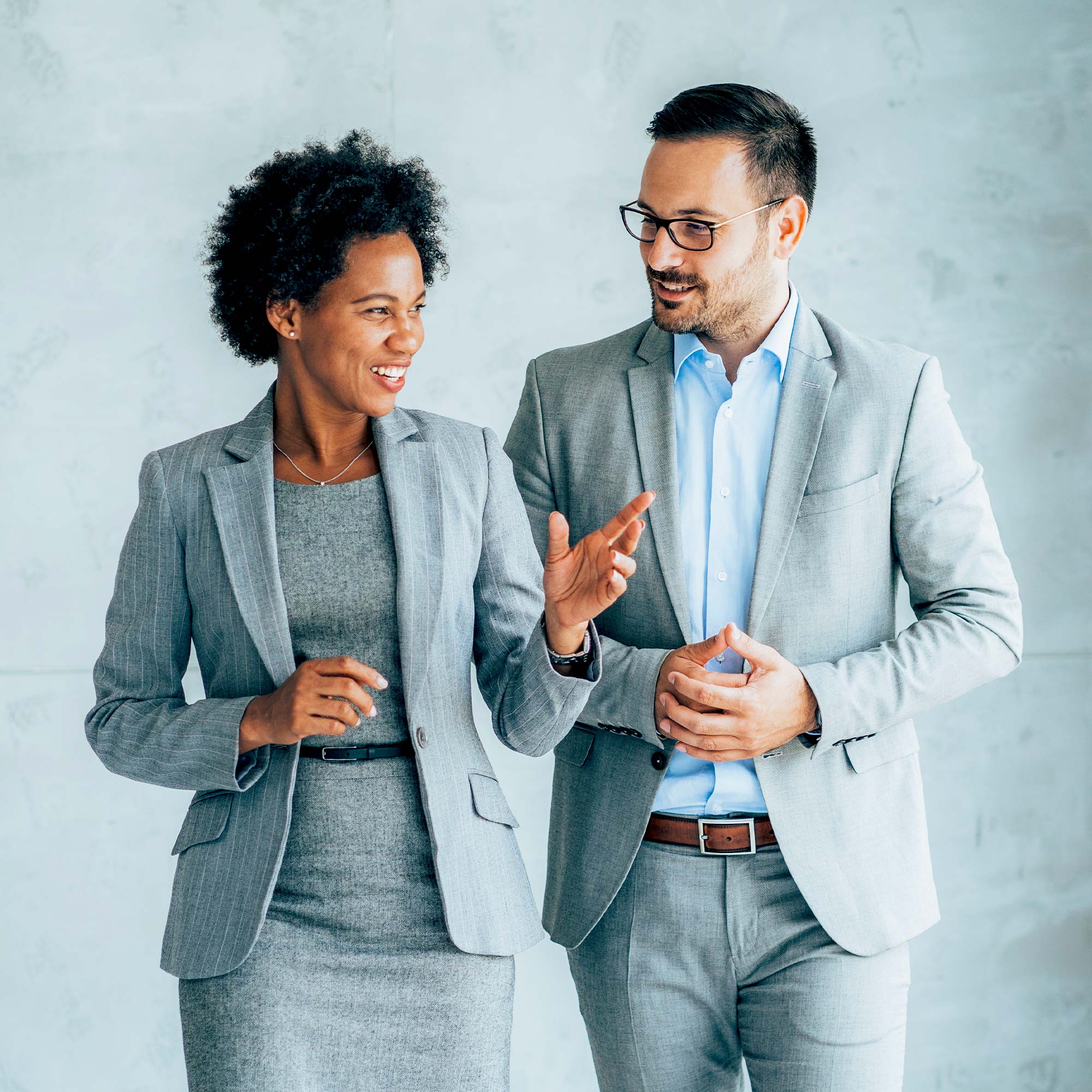 A professionally dressed man and woman wearing gray suits walk and talk.