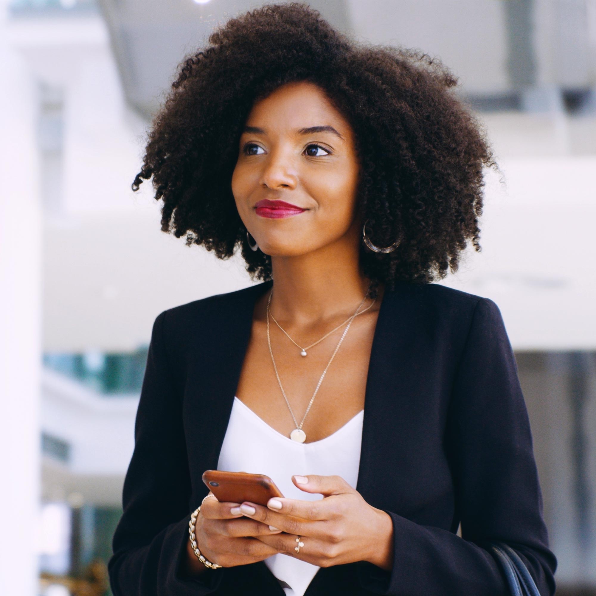A woman in a blue business jacket talks on her cell phone in front of her laptop.