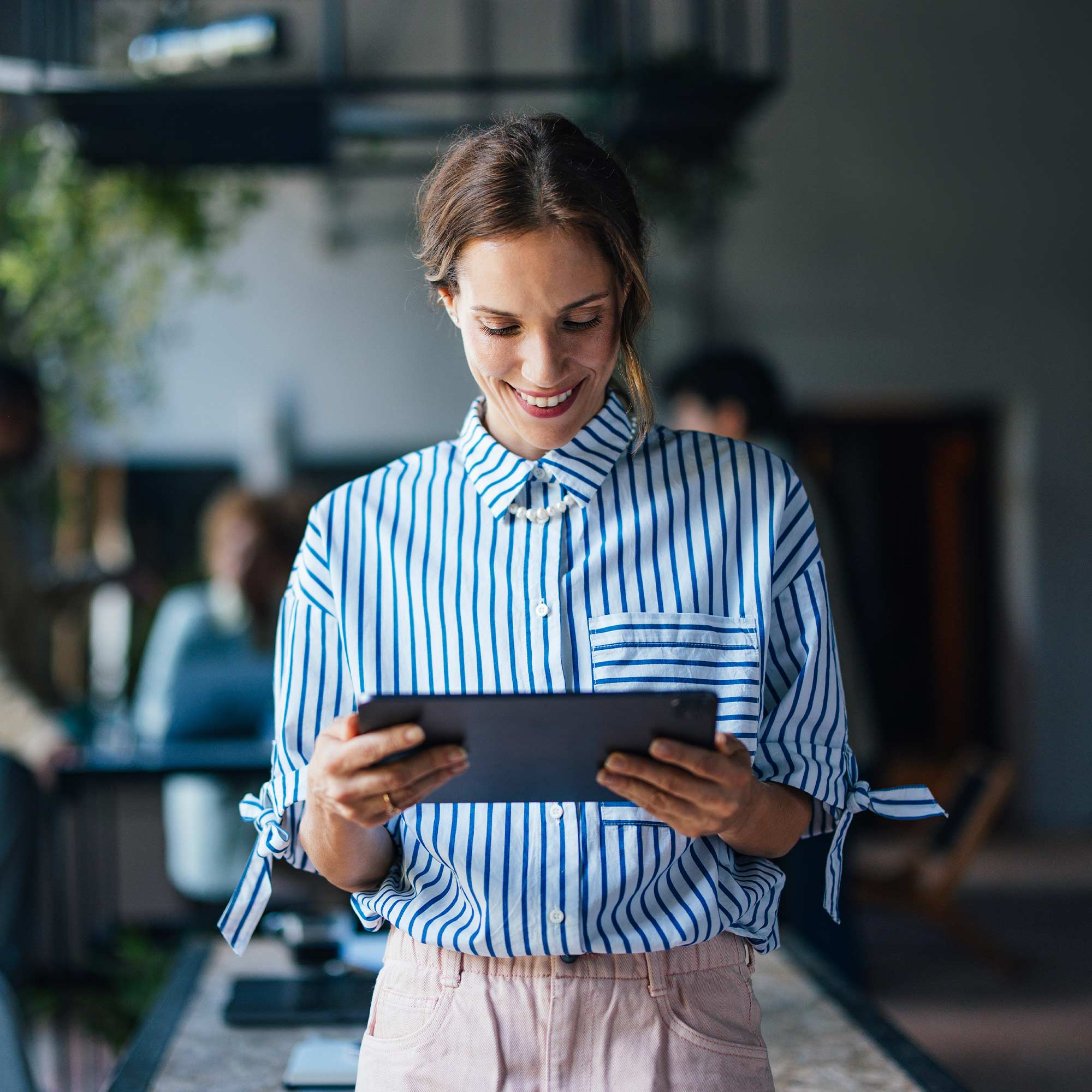 A businesswoman stands in a lobby typing on her cell phone.