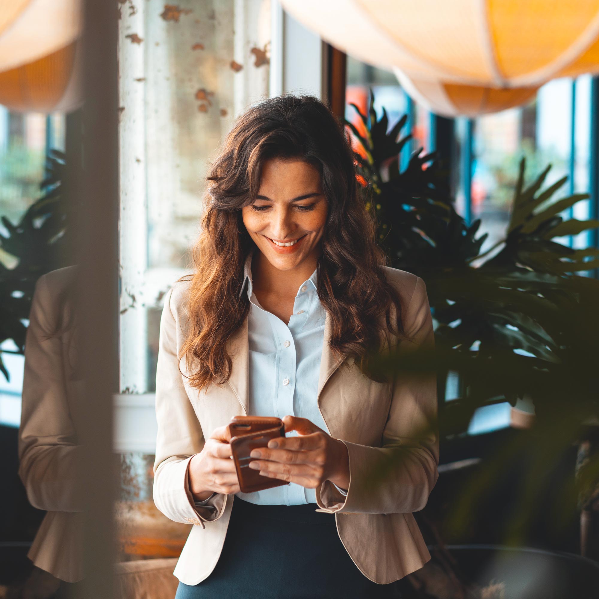 A businesswoman stands in a lobby typing on her cell phone.