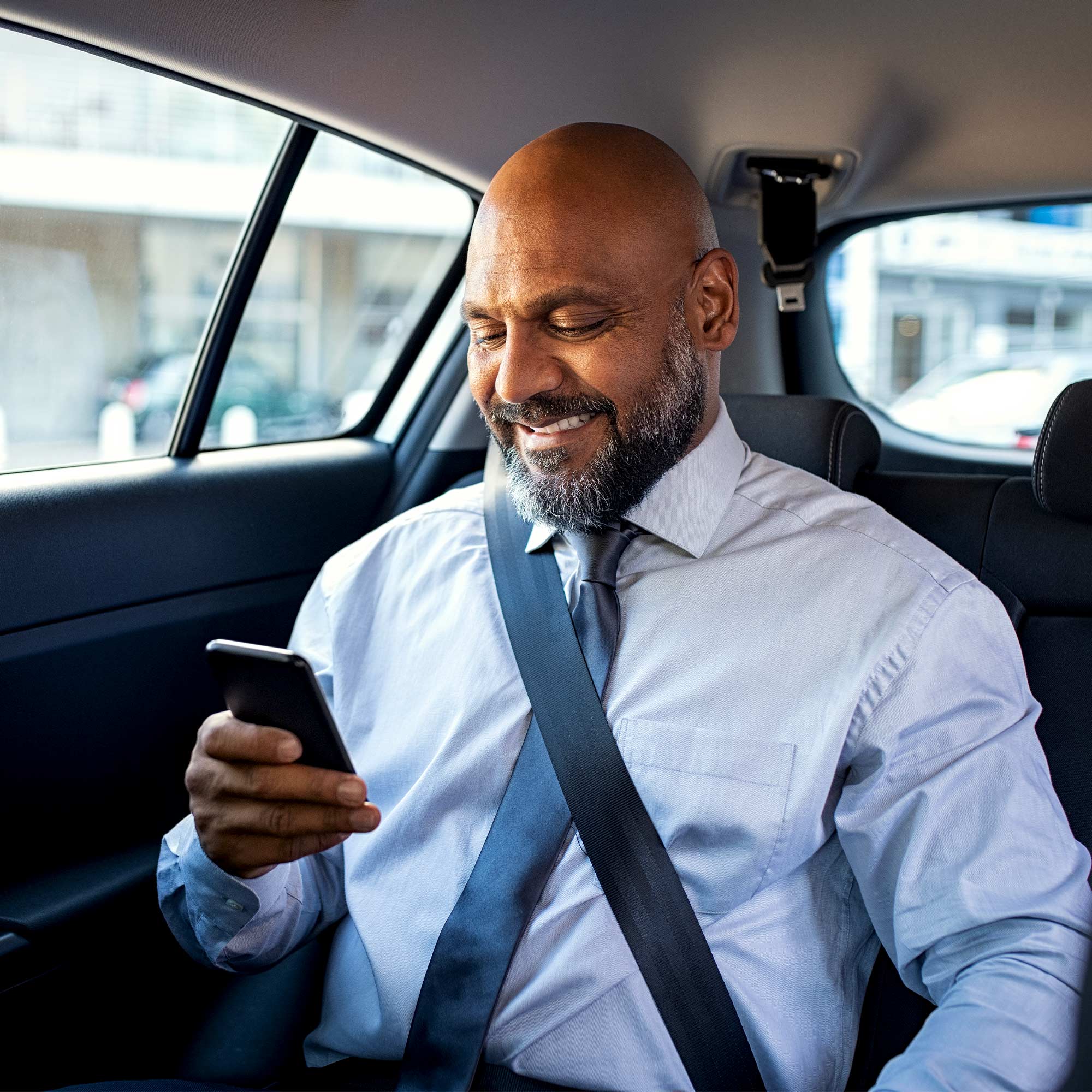 A man smiles at his phone as he sits in a vehicle.