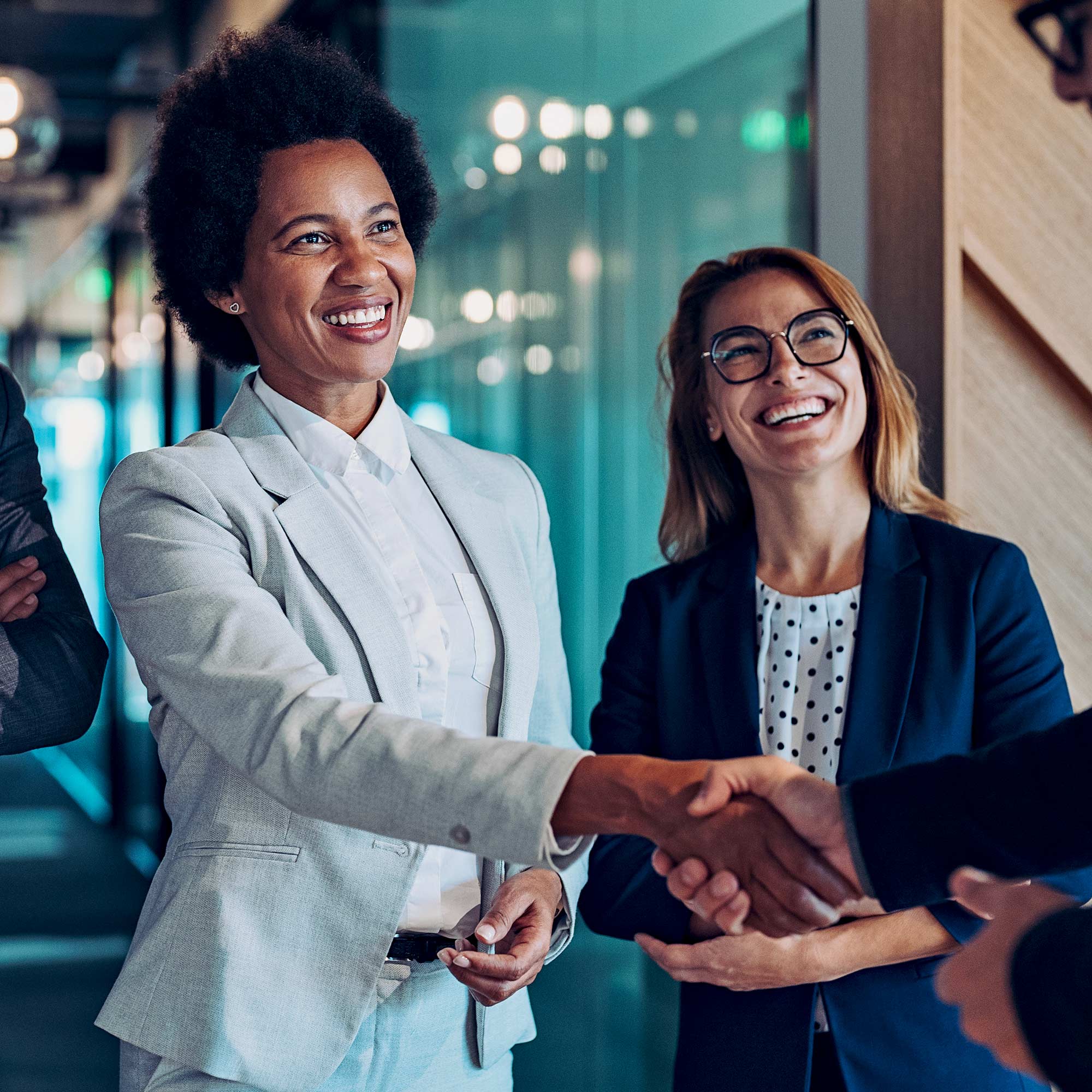 Two women shake hands with someone and smile as they are greeted.
