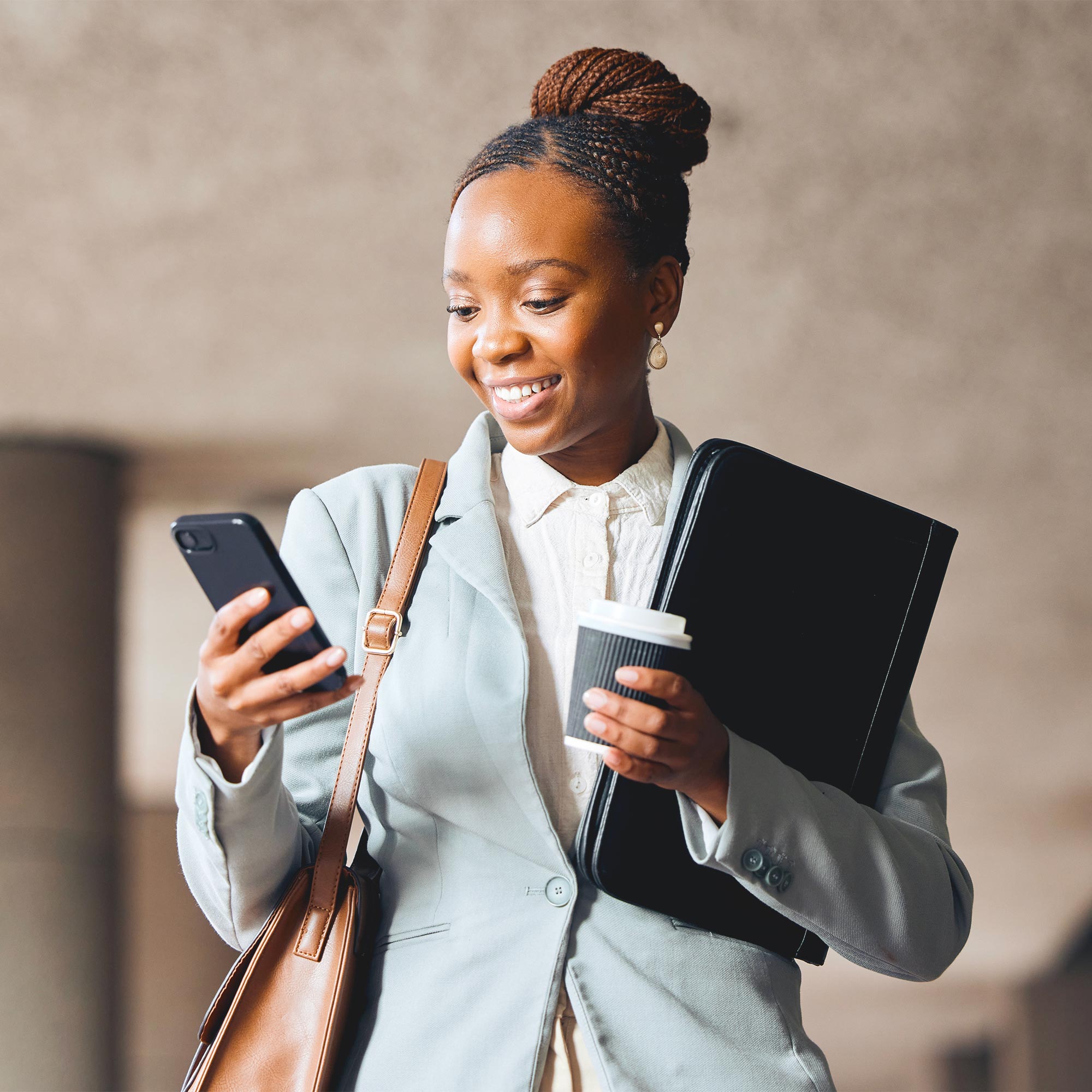 A woman in a business suit carries her notebook and smiles at her cell phone.