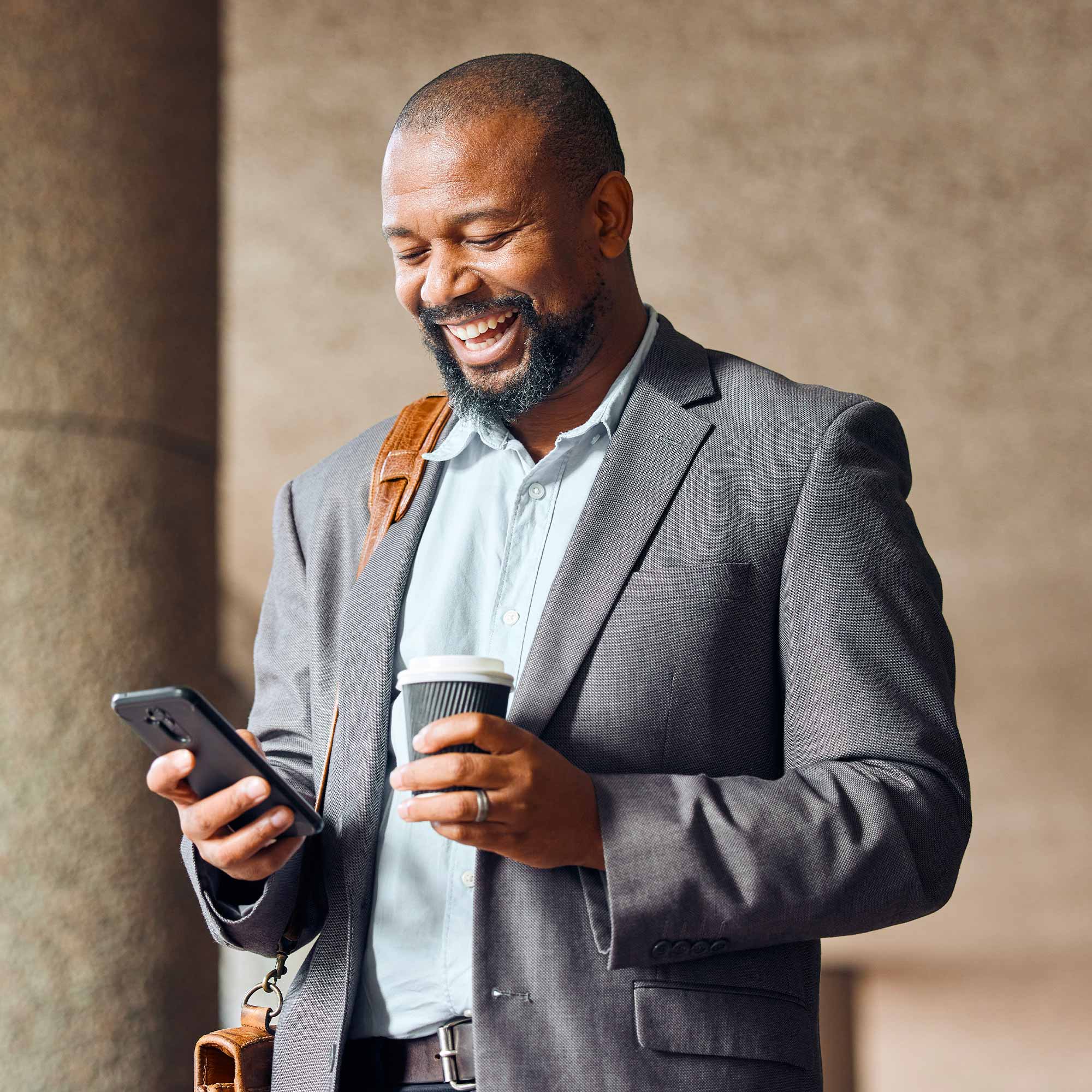 A man in a business suit stands and laughs as he looks at his cell phone.