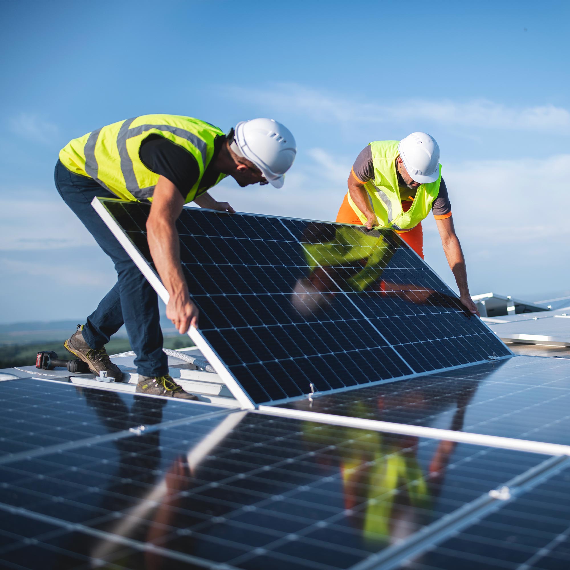 Two men lift solar panels onto a roof.
