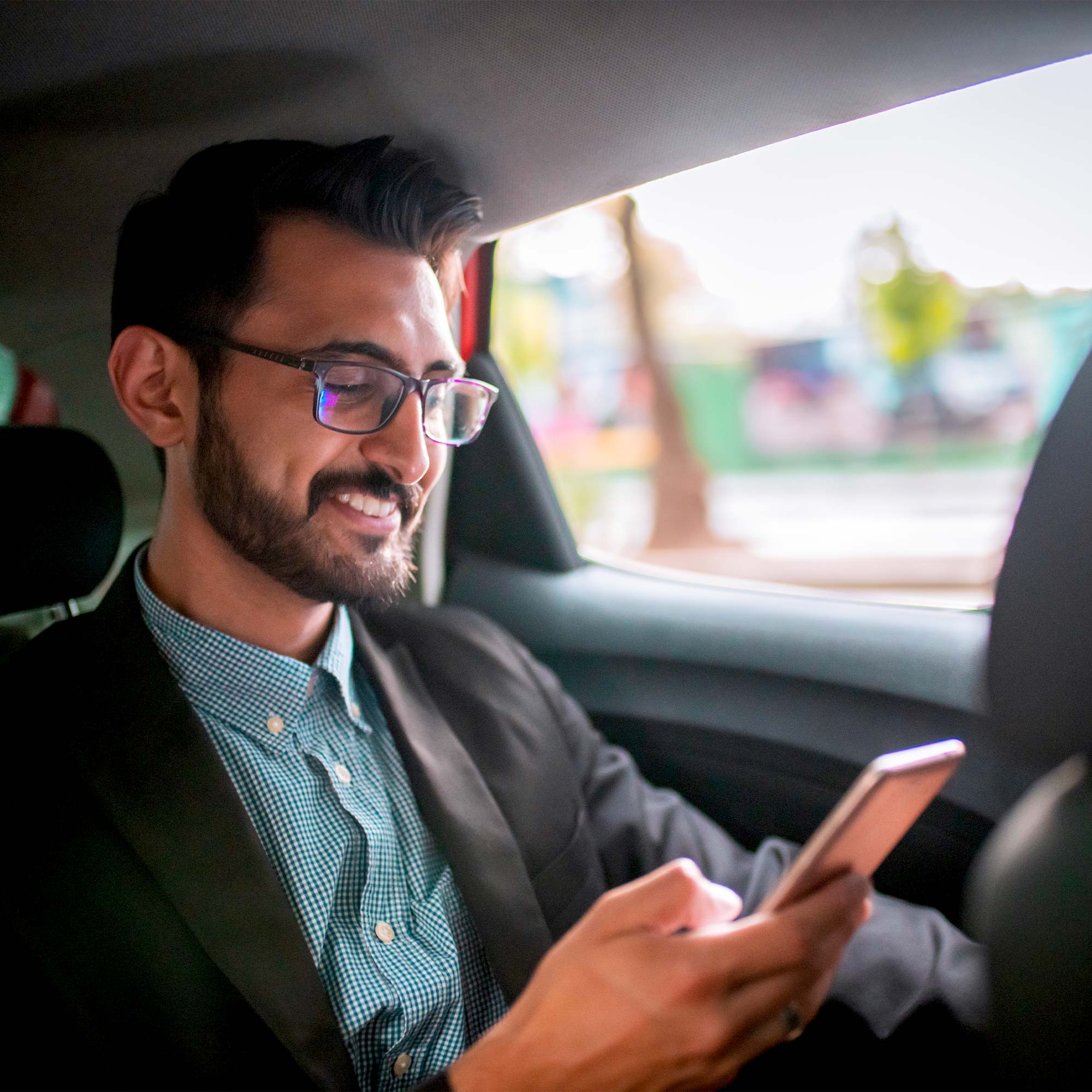 A man sitting in a car uses his cell phone and smiles.