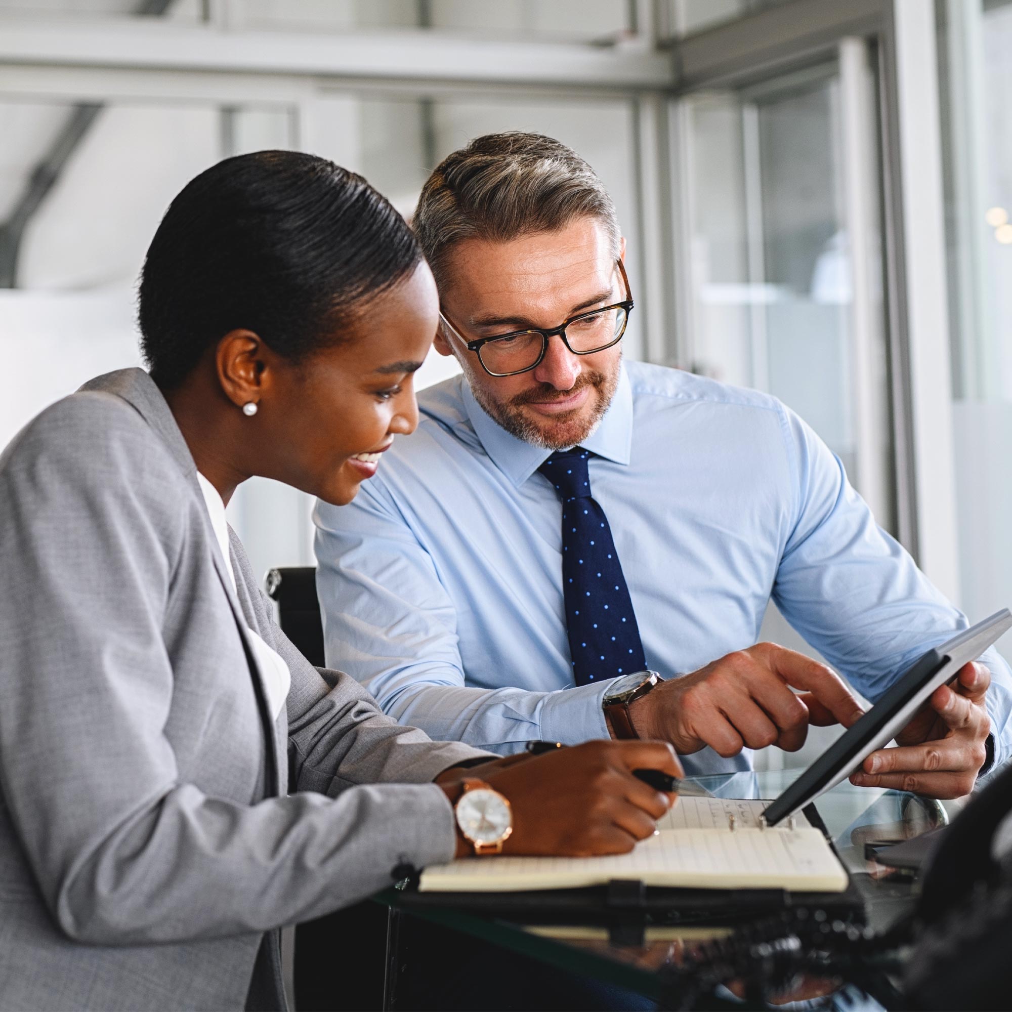 Two professionally dressed people sitting at a desk and using a tablet