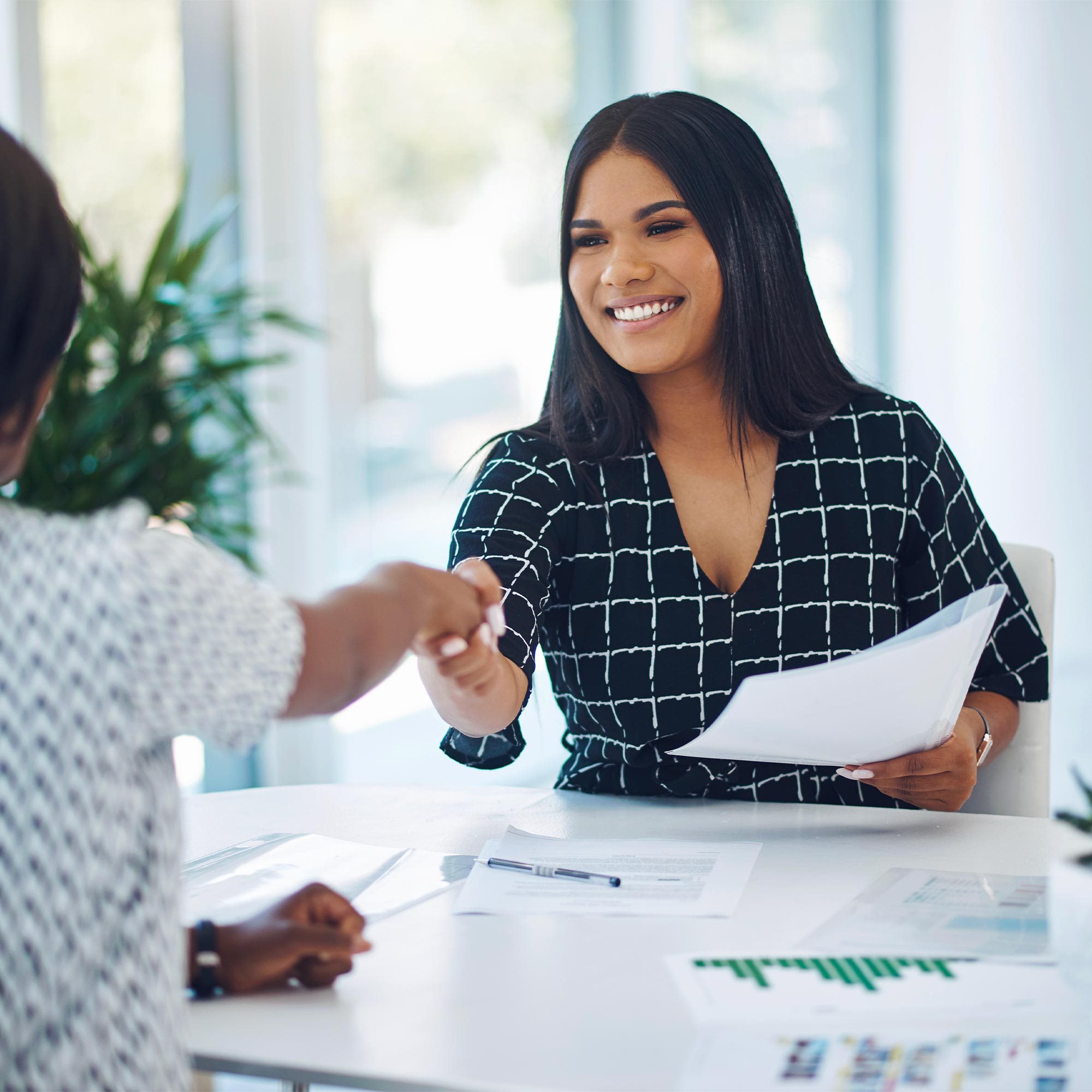 A woman smiles and shakes someone's hand across the desk.