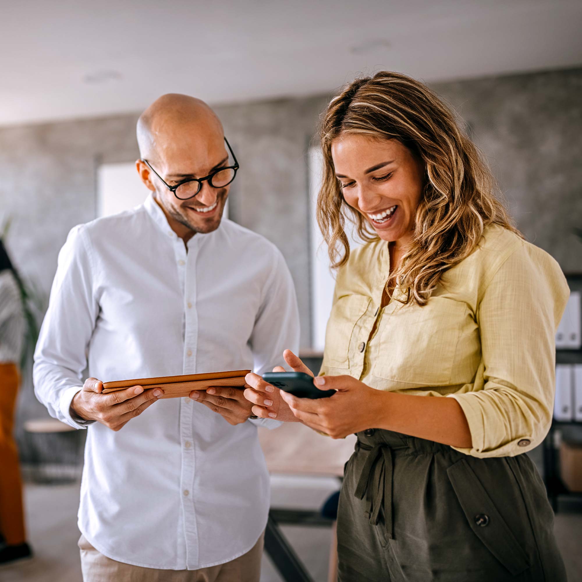 A man and woman smile as they look at a cell phone.