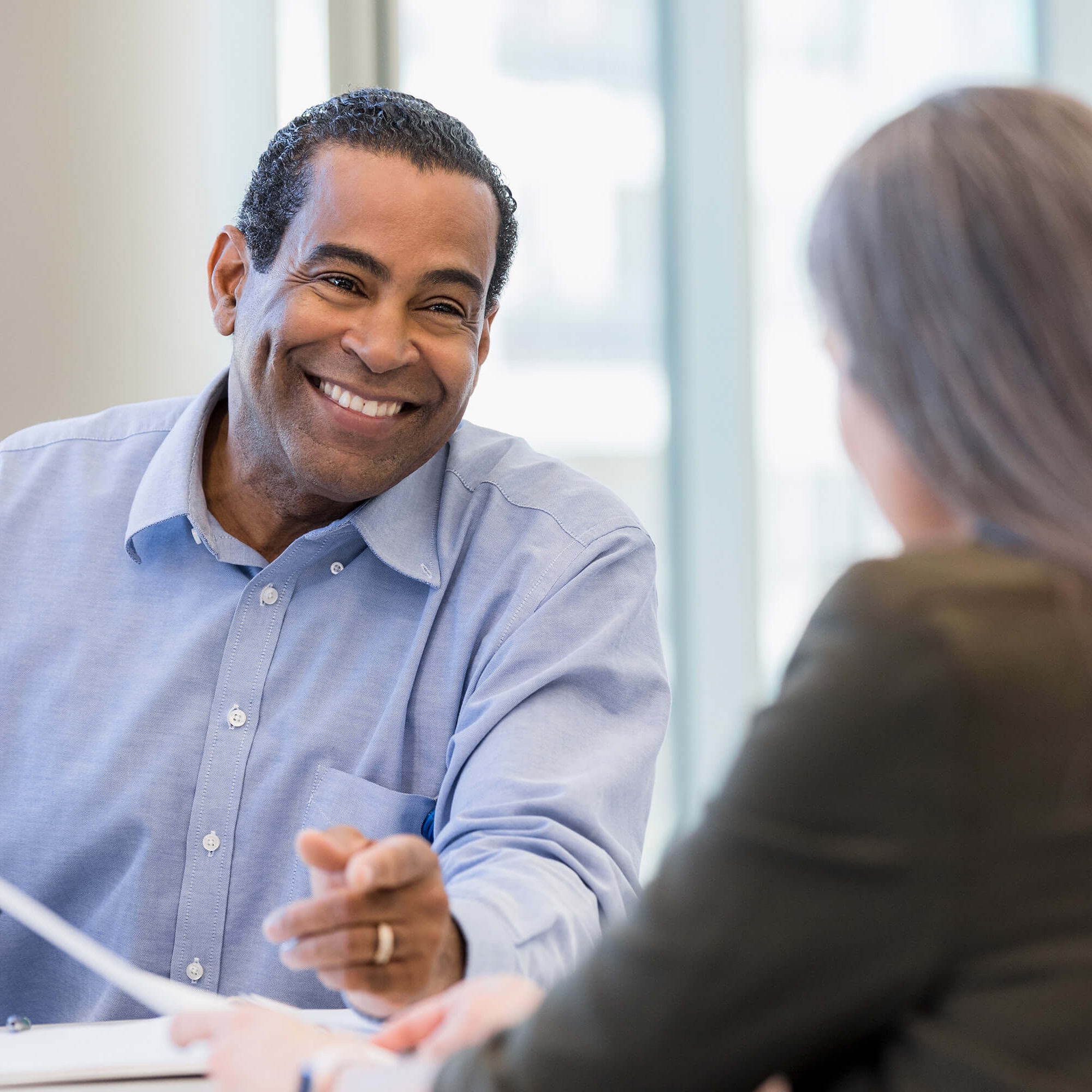 A man in a blue button up shirt smiles at a woman sitting across the desk.
