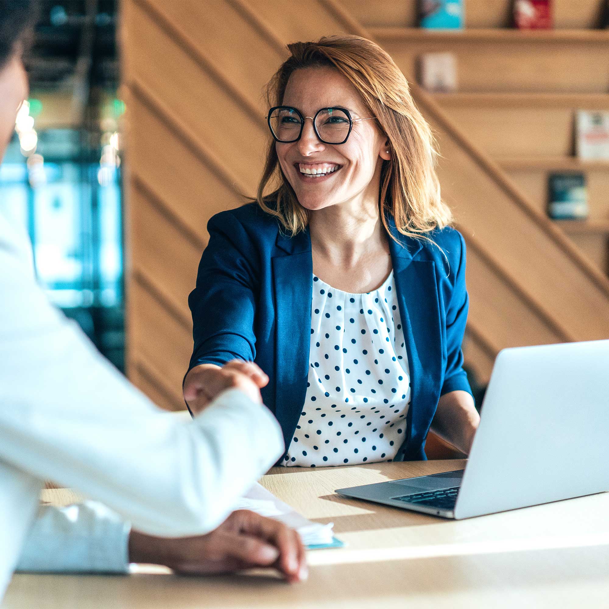 Woman holding a resume talking to another woman at a table with a laptop