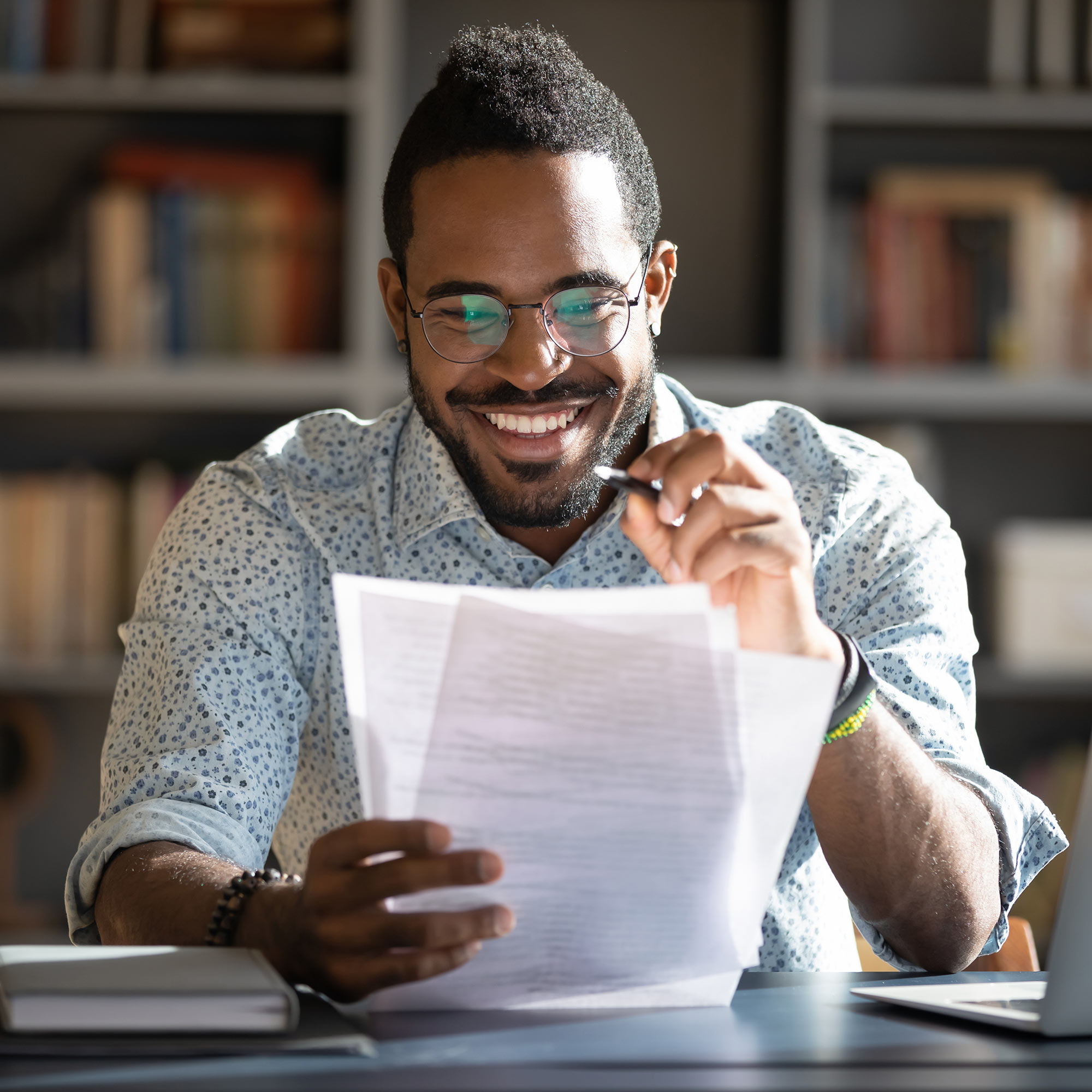 Man wearing blue button up shirt and glasses smiling and talking to two other professionally dressed people about his resume