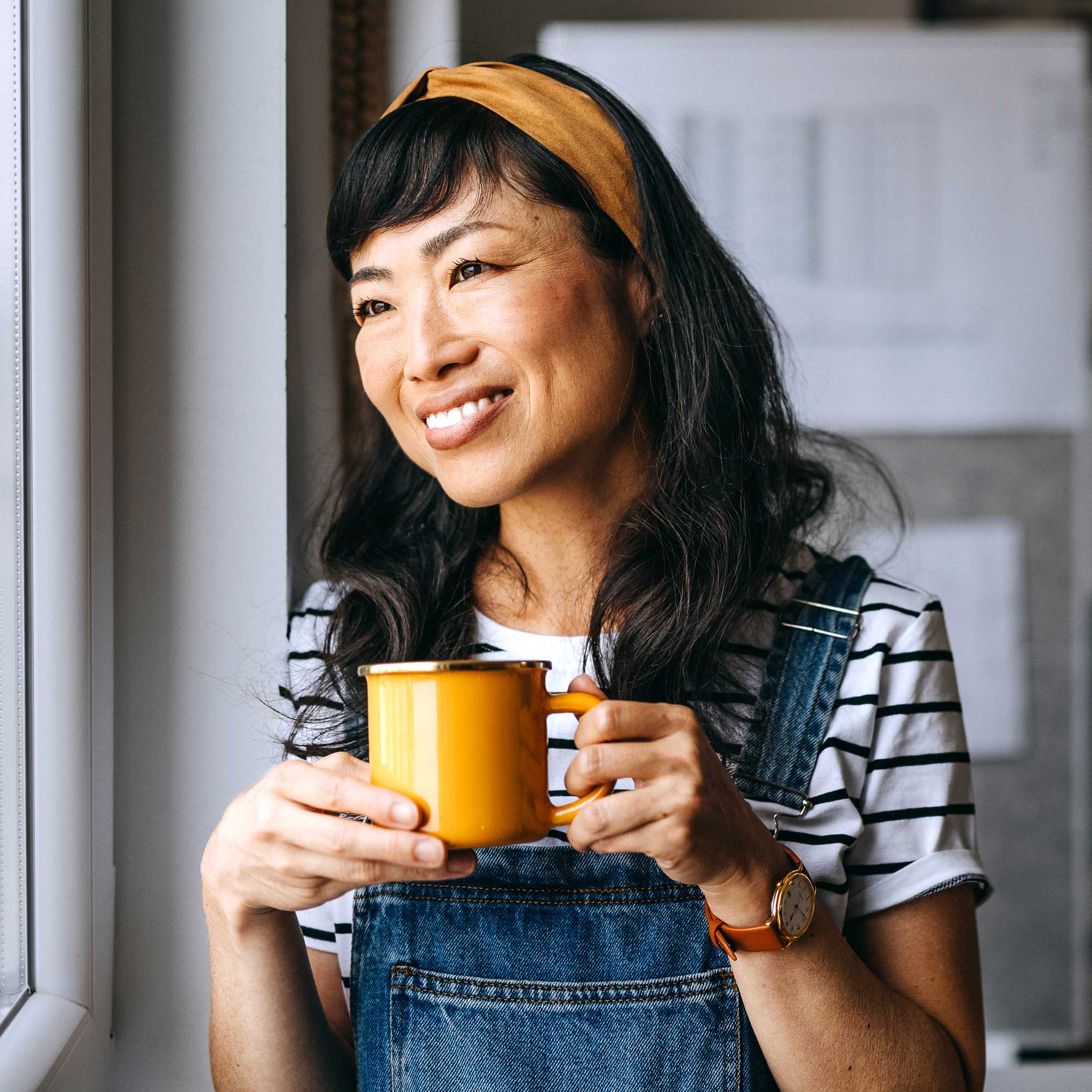 A woman with an orange coffee cup smiling and looking out the window.