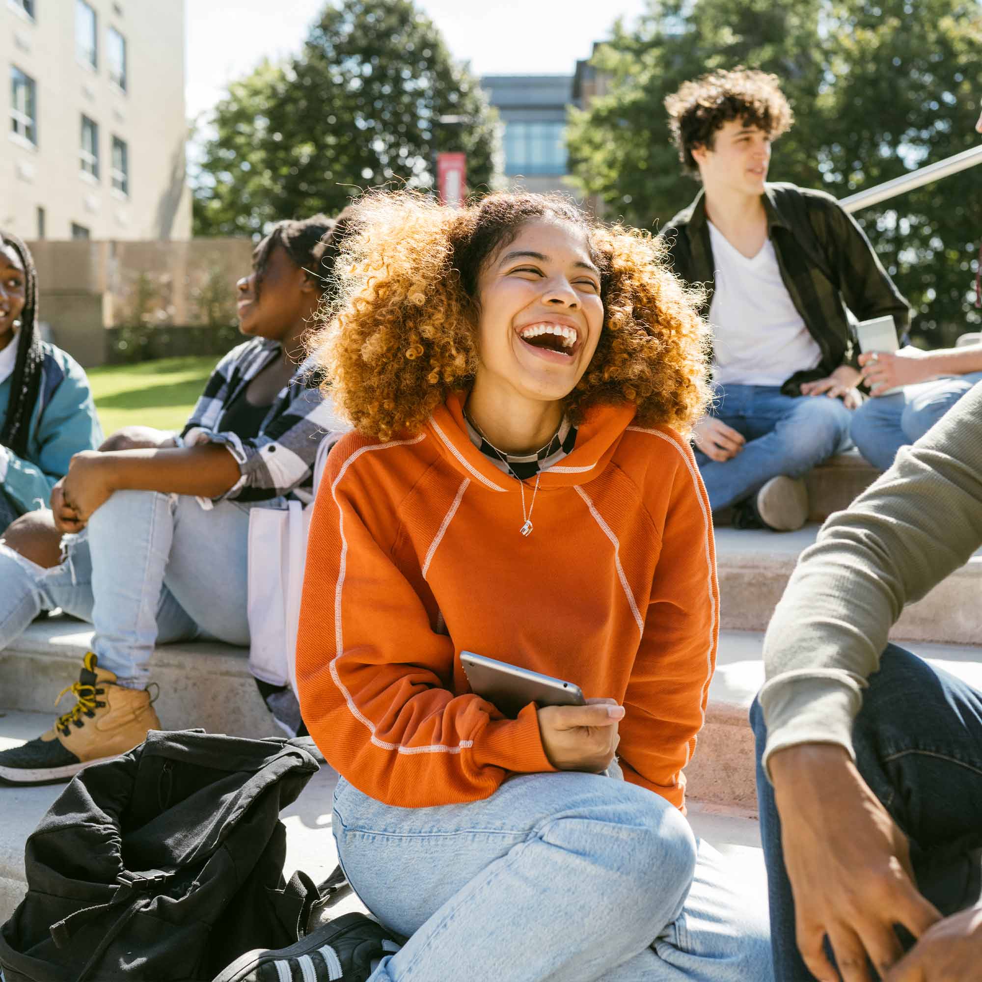 A woman in an orange hoodie laughing with a group of friends on a college campus