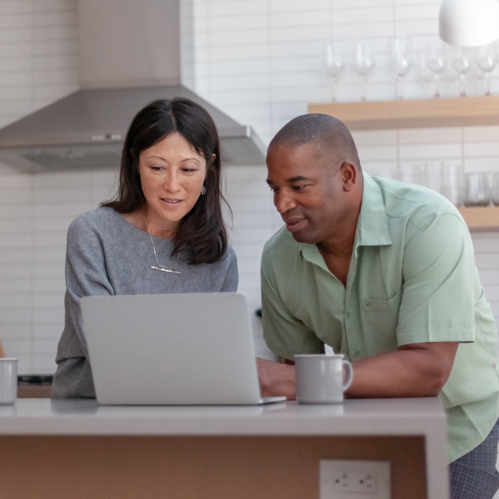 Man and woman leaning on their kitchen countertop and looking at a laptop