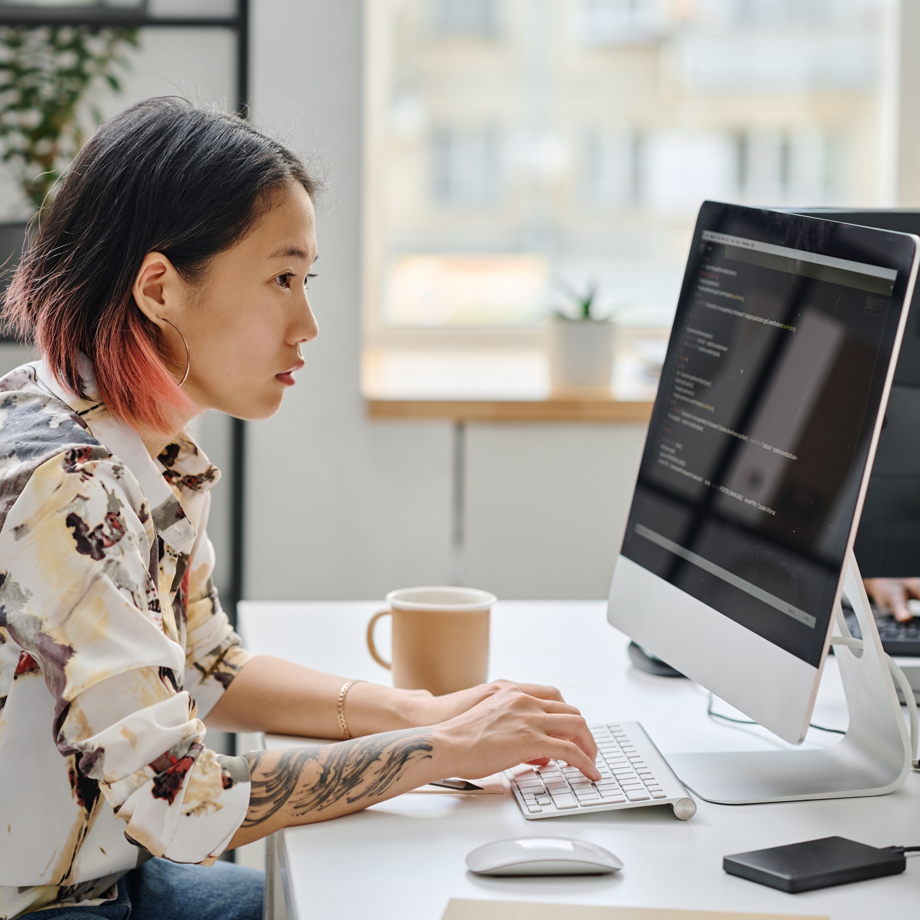 Woman sitting at a desk with a cup of coffee using her computer to look at code