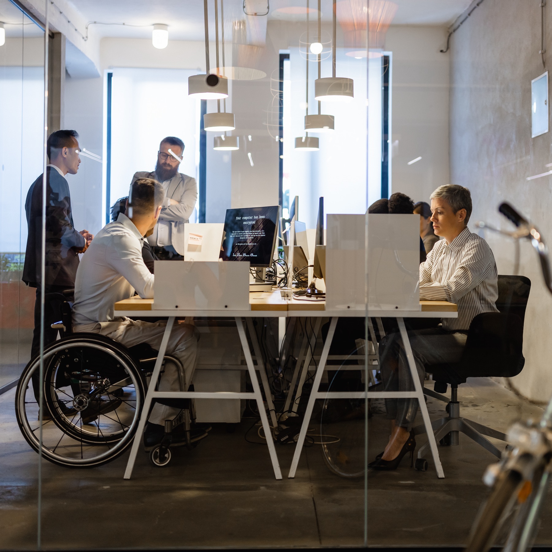 A group of business workers sitting and standing around some desks and discussing work on a computer