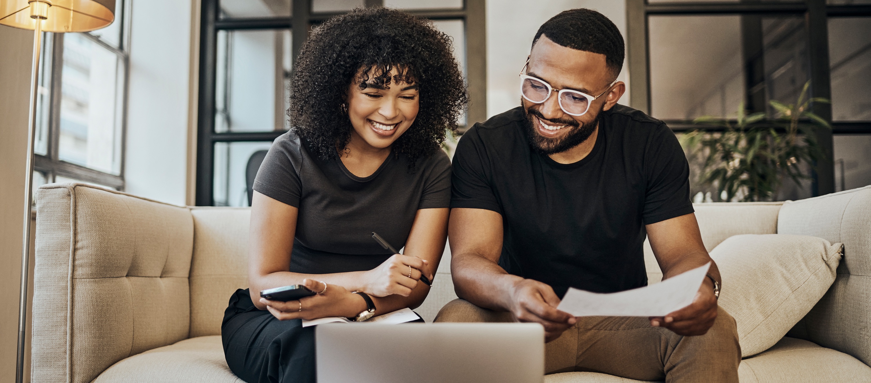 Man and woman sitting on a couch in their living room smiling at a laptop