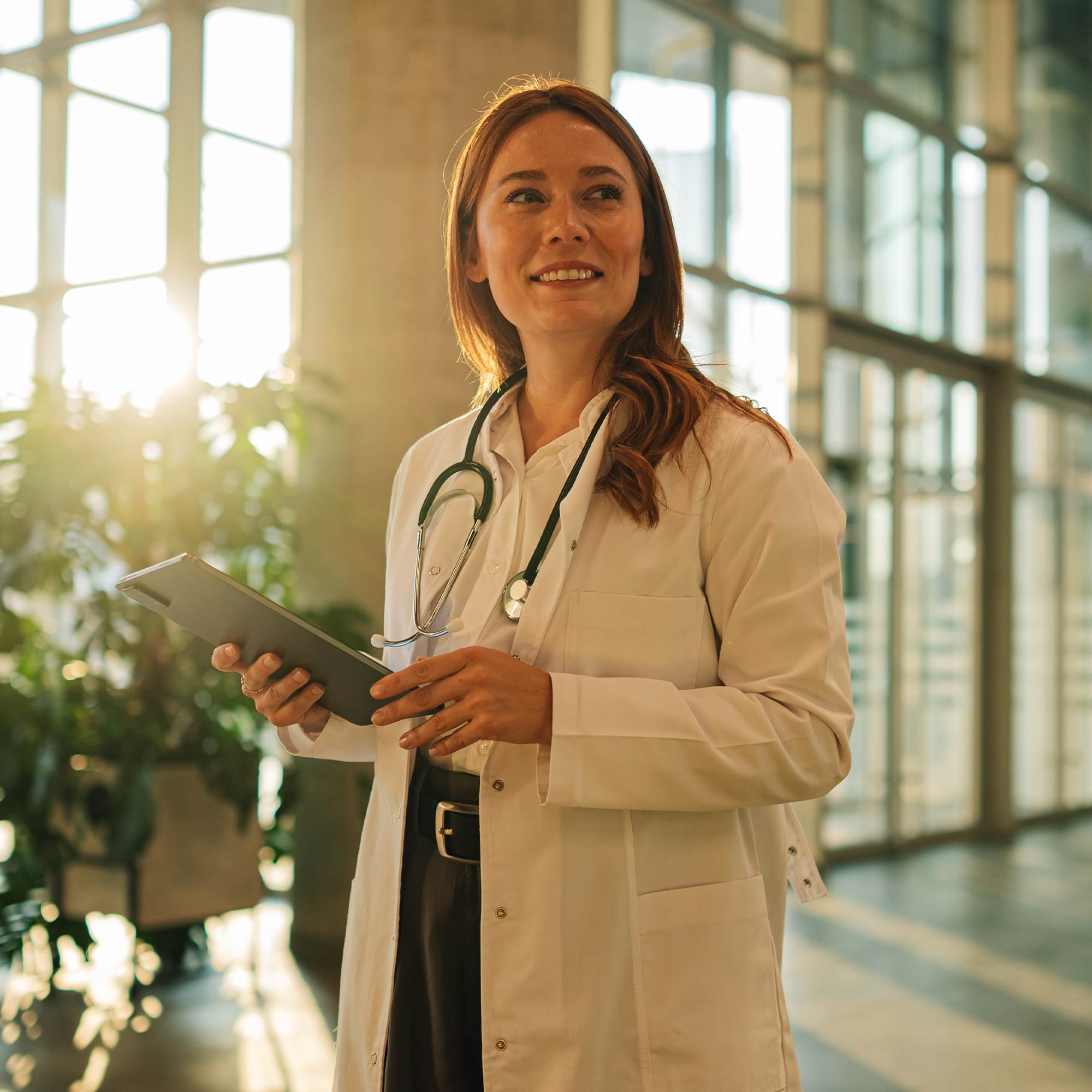 A doctor wearing a stethoscope, smiles as he looks a tablet.