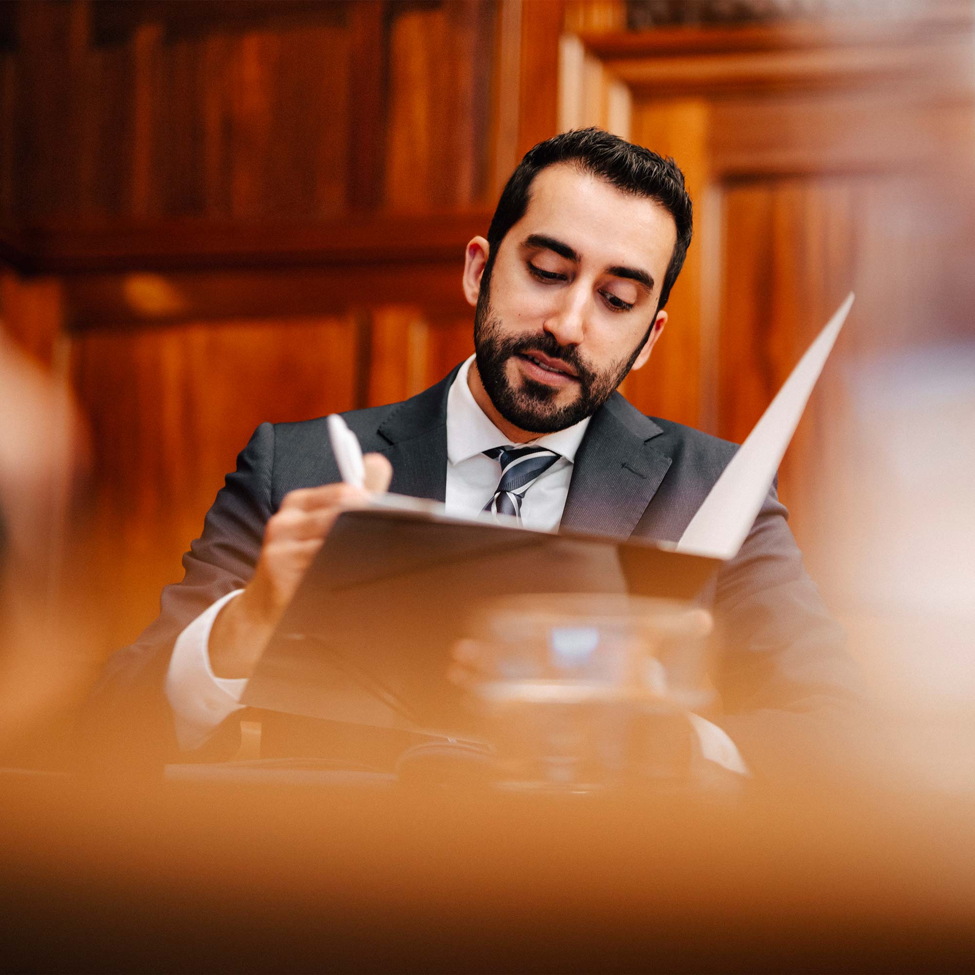 Man in formal attire writing with a pen on a clipboard in an attorney's office