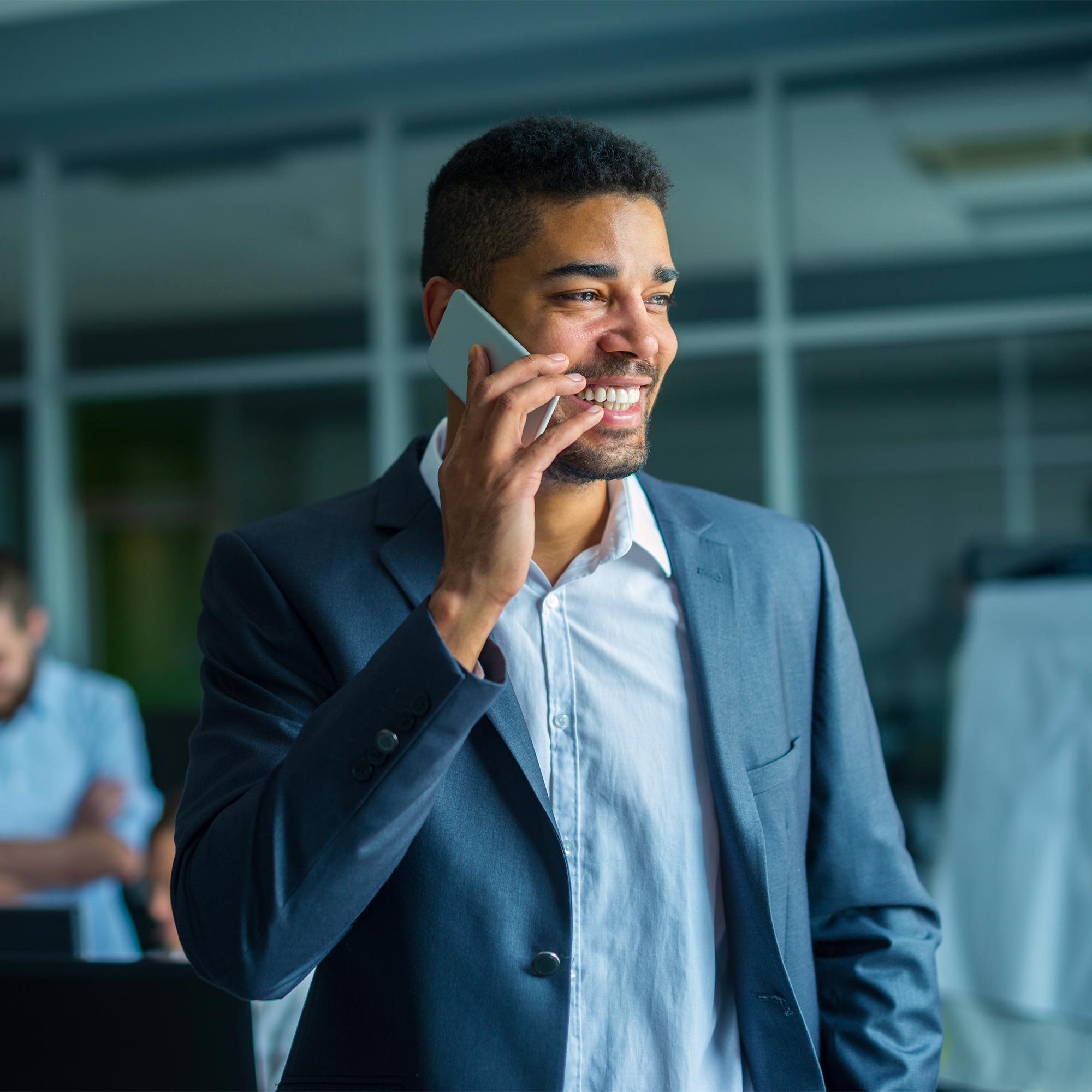 A professionally dressed man talks on the phone and smiles.