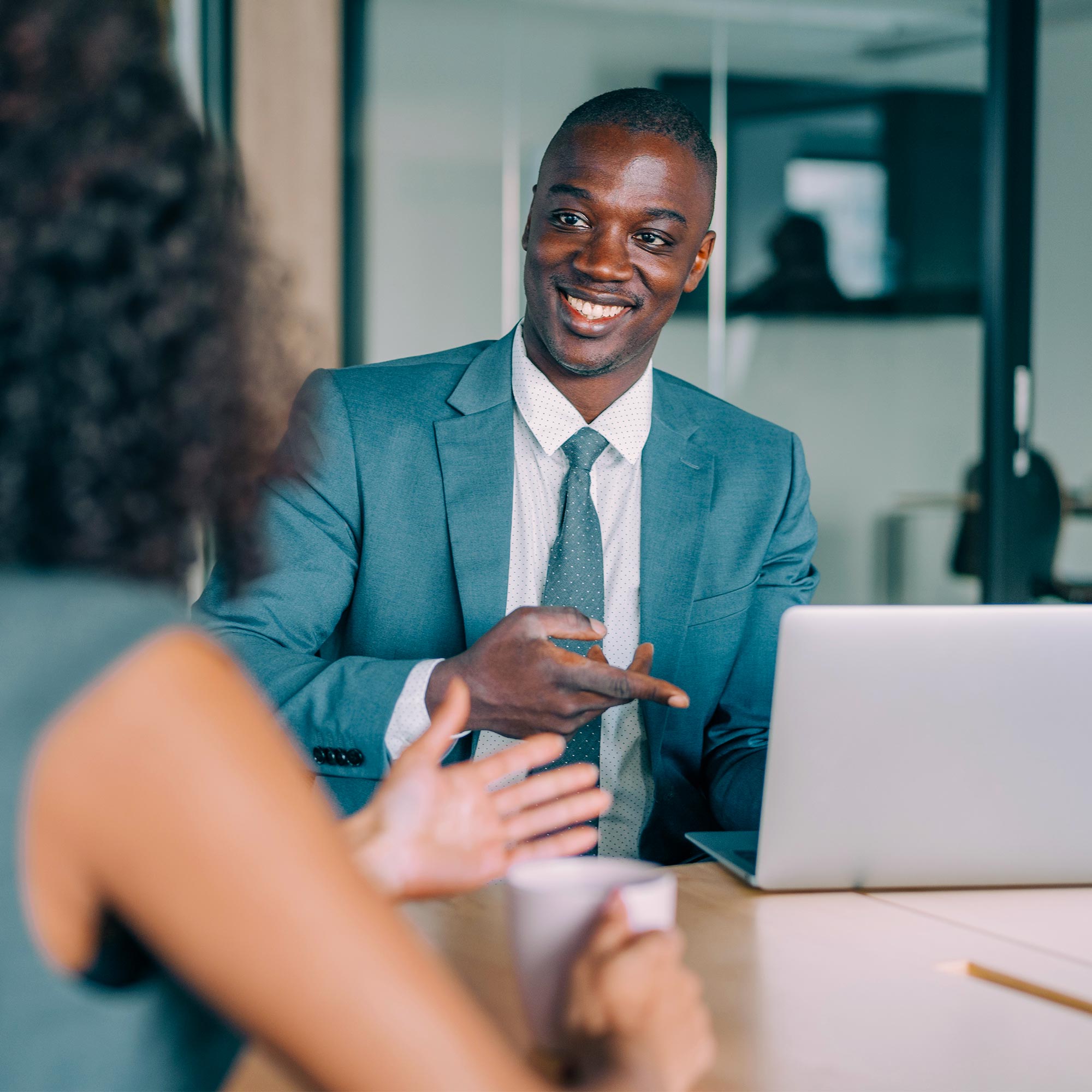 A man in a business suit points to his laptop and smiles.