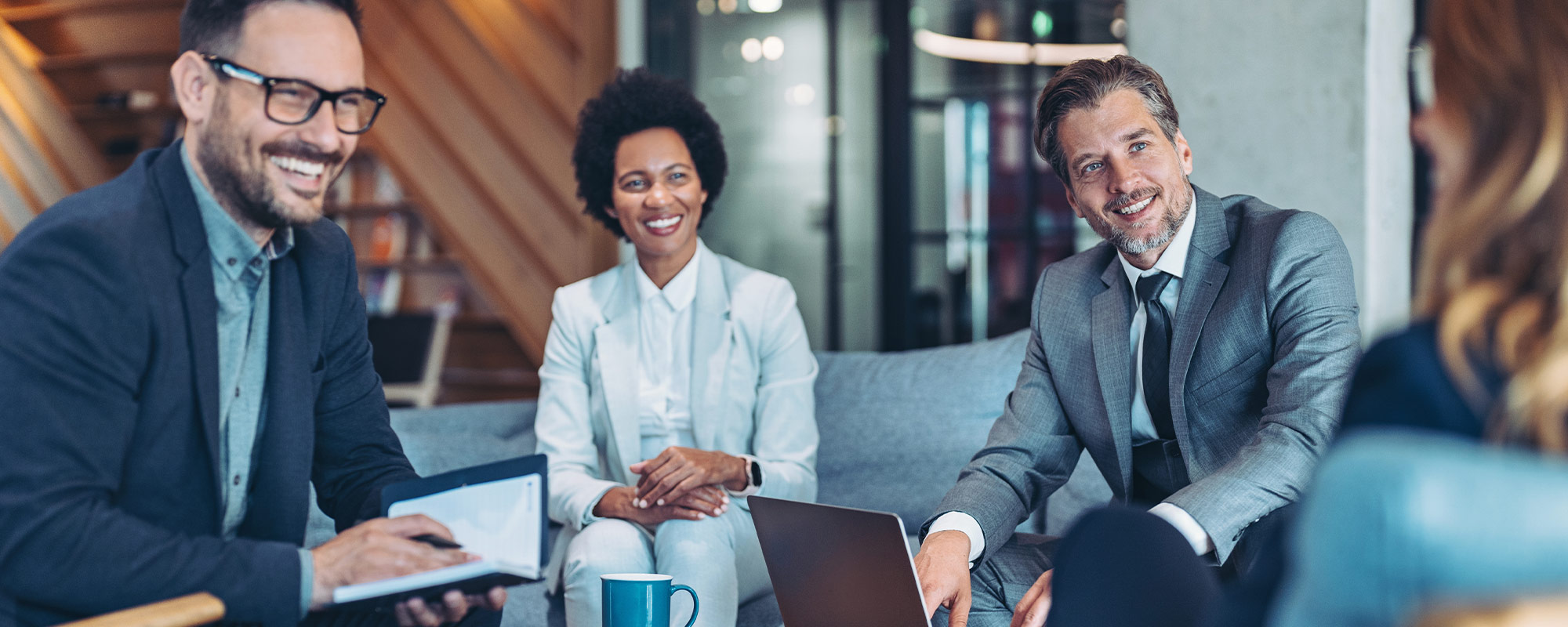 A woman and two men in business suits sitting in chairs conversing. 
