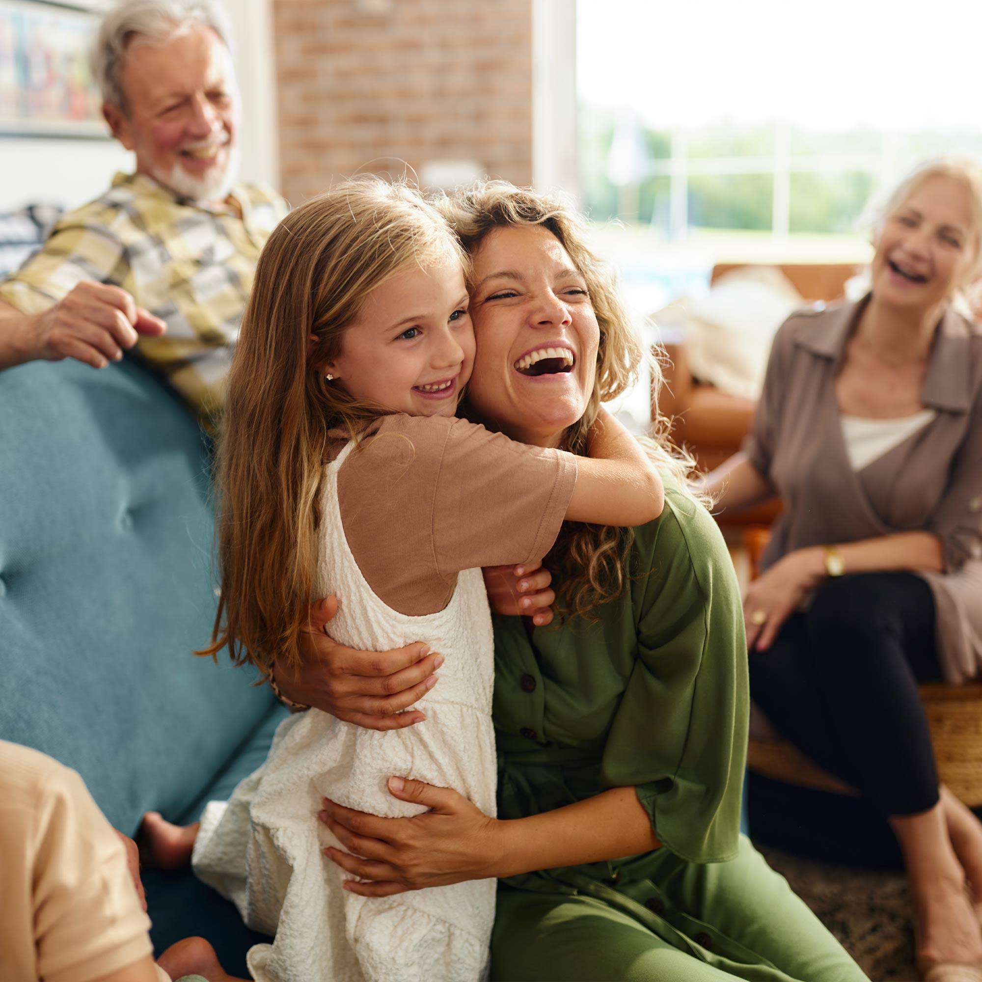 Woman in a wheelchair and another woman and child sitting on a bed smiling and looking at a laptop