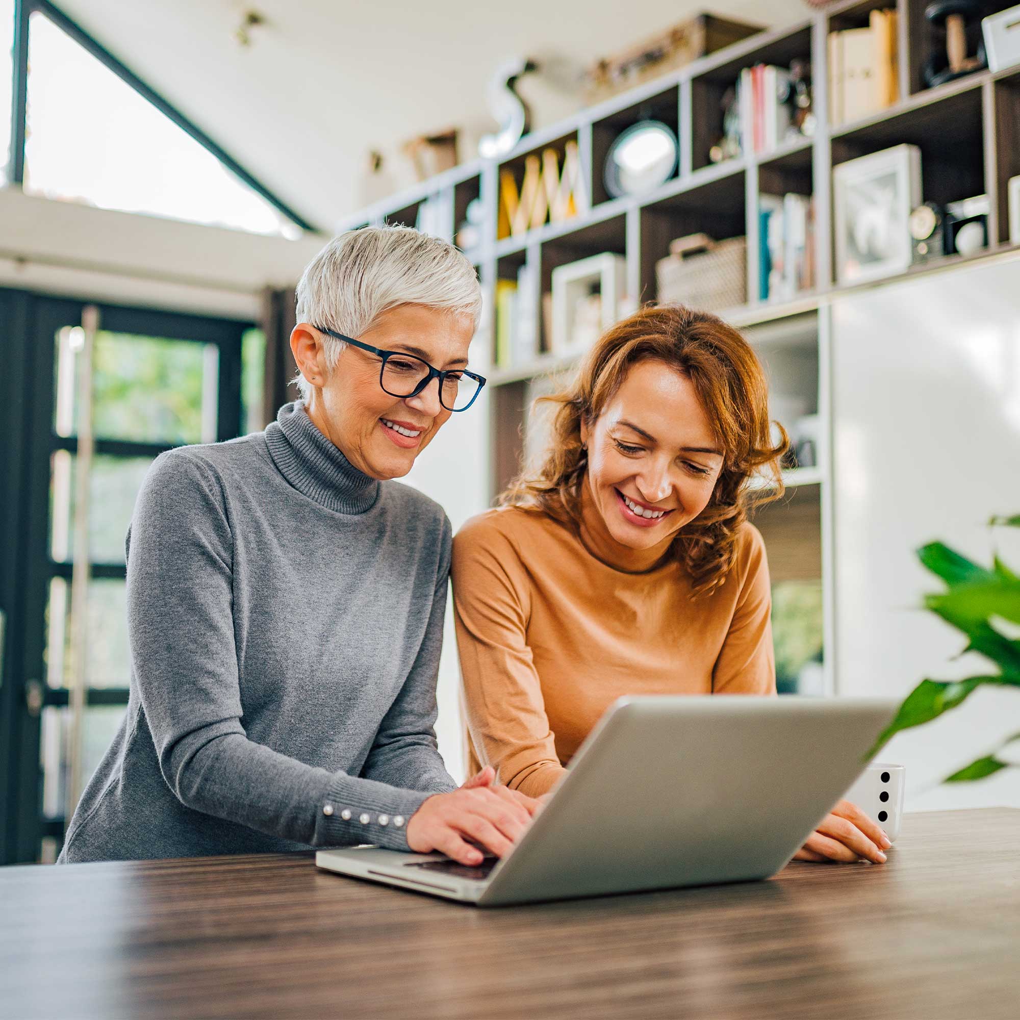 Two women stand and look at the laptop screen.