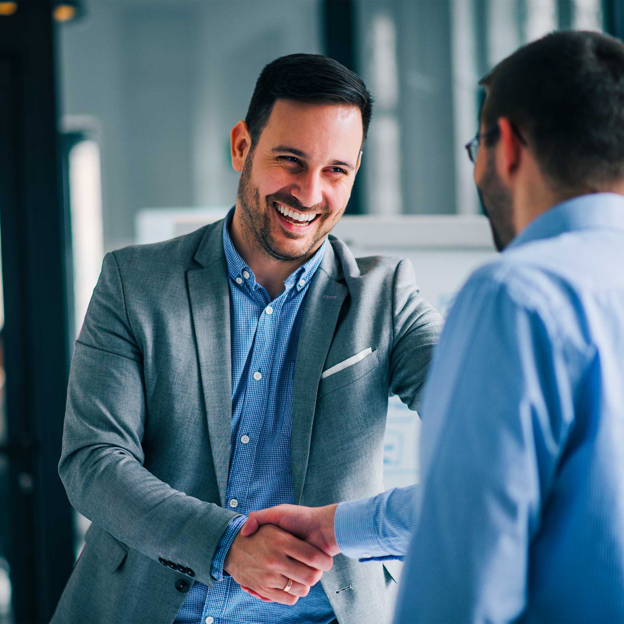 A professionally-dressed man shakes hands with another man and smiles.