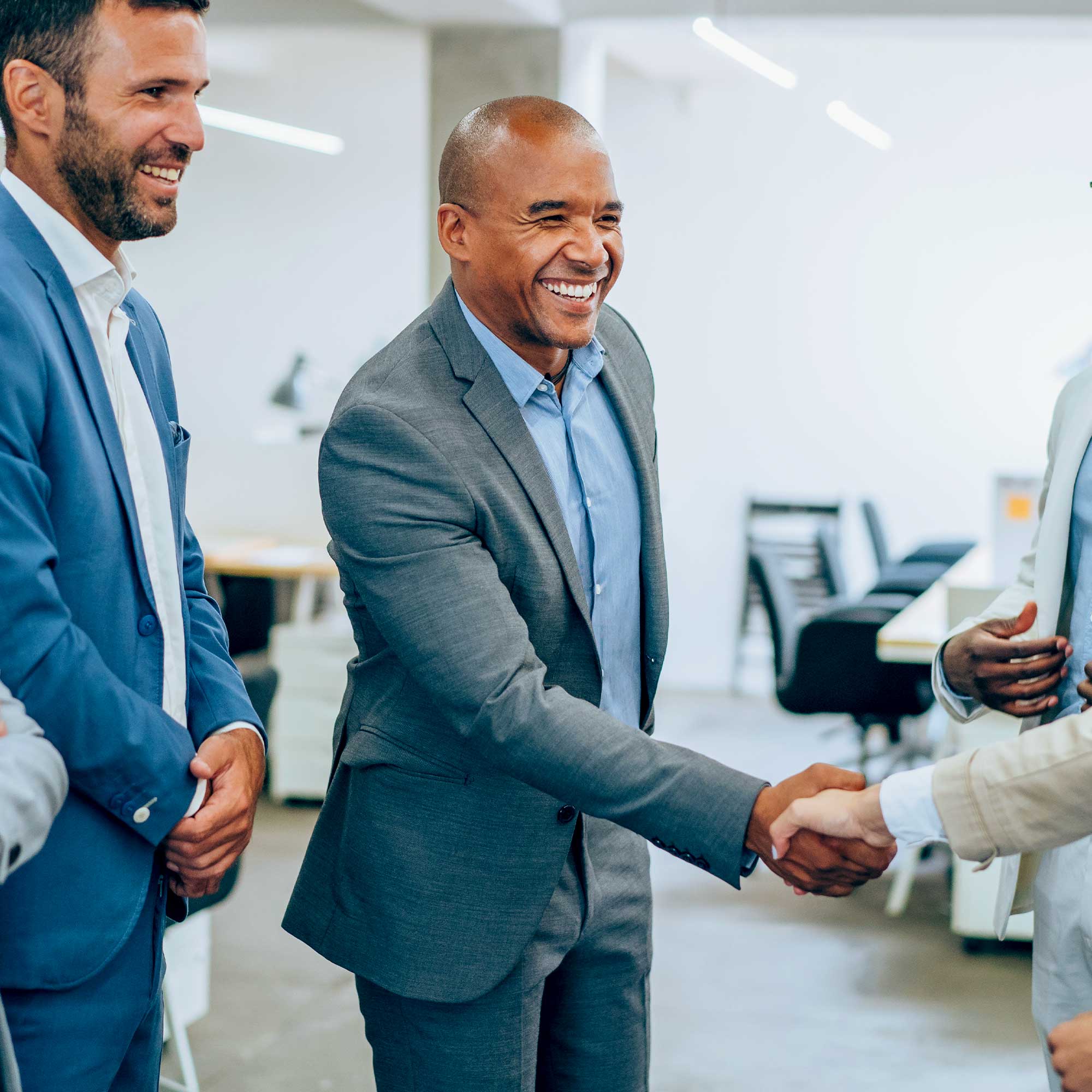 A professionally-dressed man shakes hands with another man and smiles.
