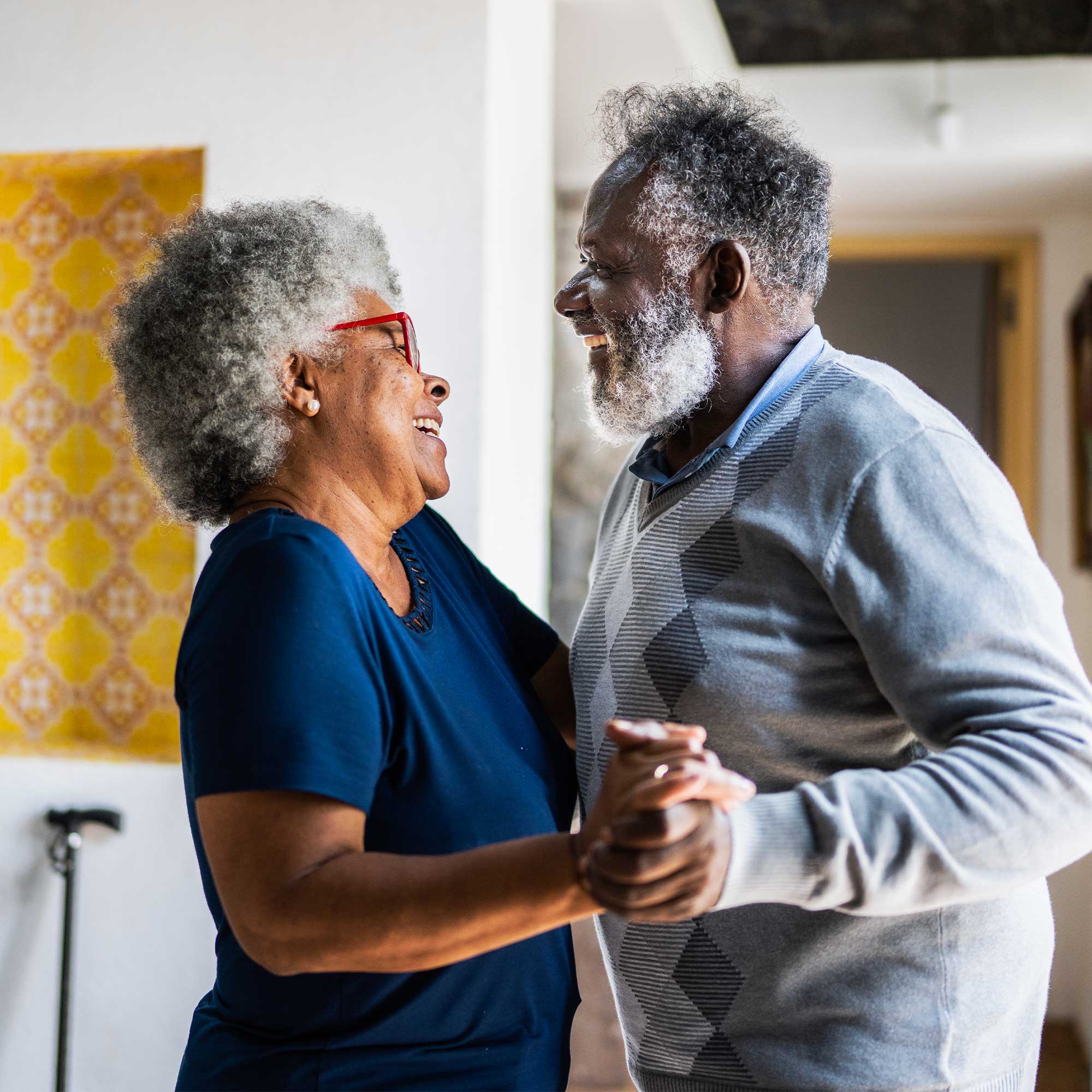 Older man and woman smiling and dancing in their living room.