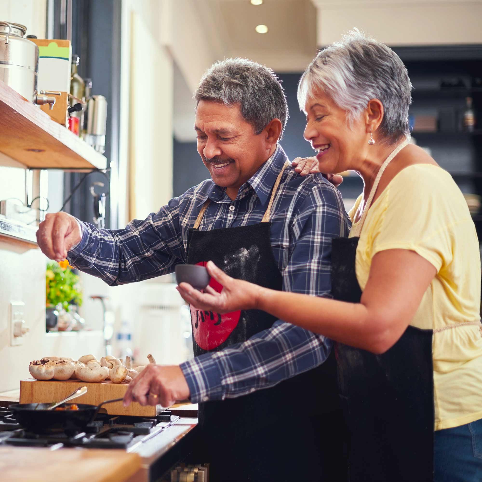 A man and woman in aprons are cooking in the kitchen.