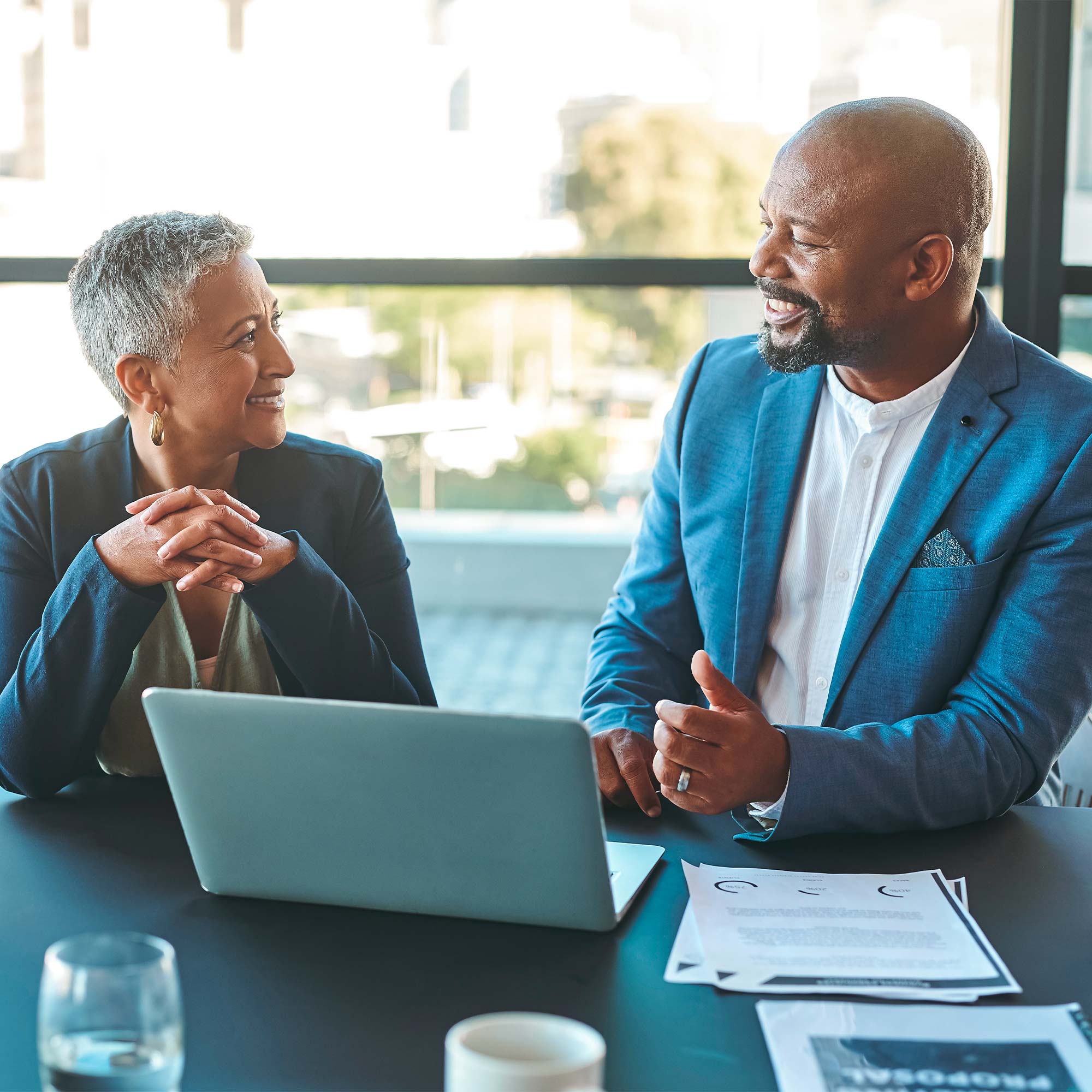 A man haves a discussion with a woman as they sit near in front of the laptop.