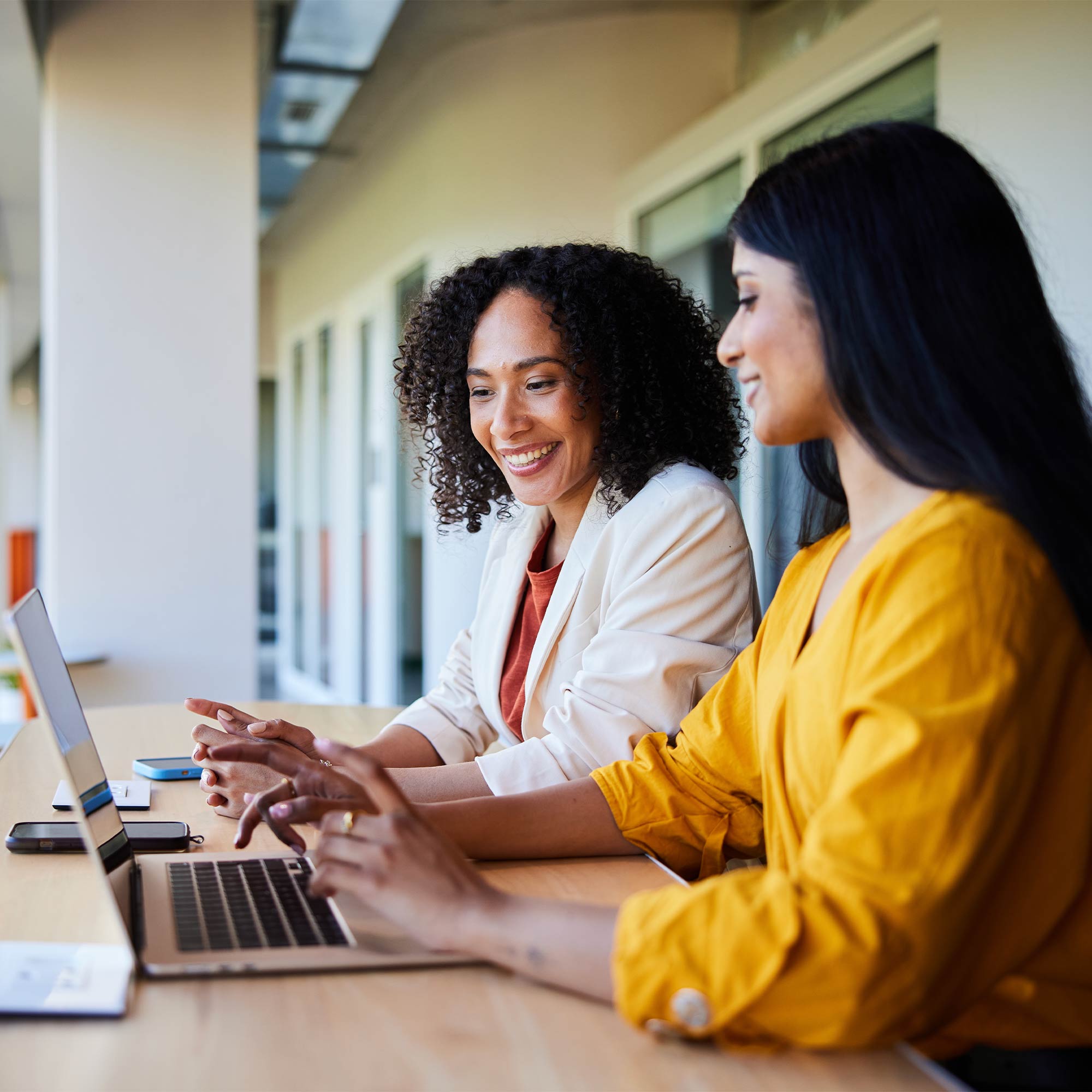 Two professionally dressed women talking to each other while sitting at a wooden table