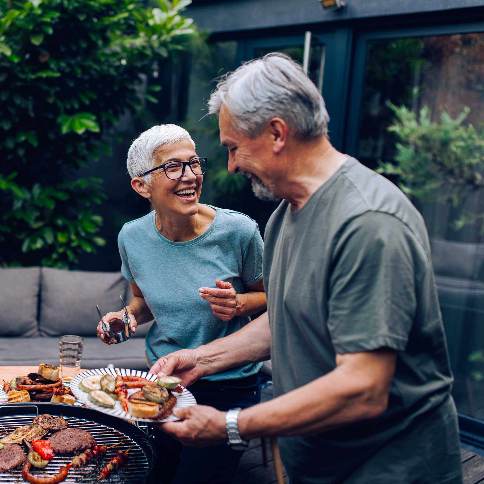Elder woman and man smiling as they grill out. 