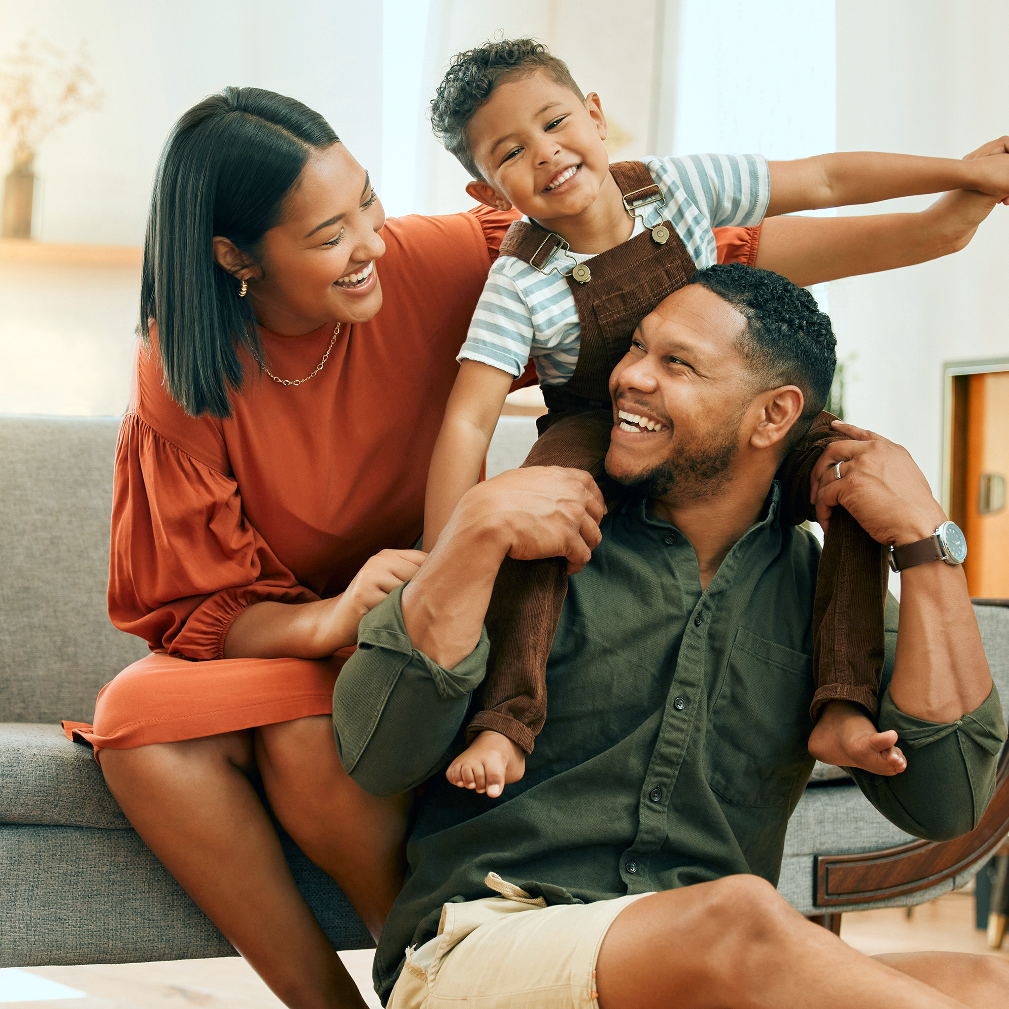 A smiling family of three sitting in their living room.
