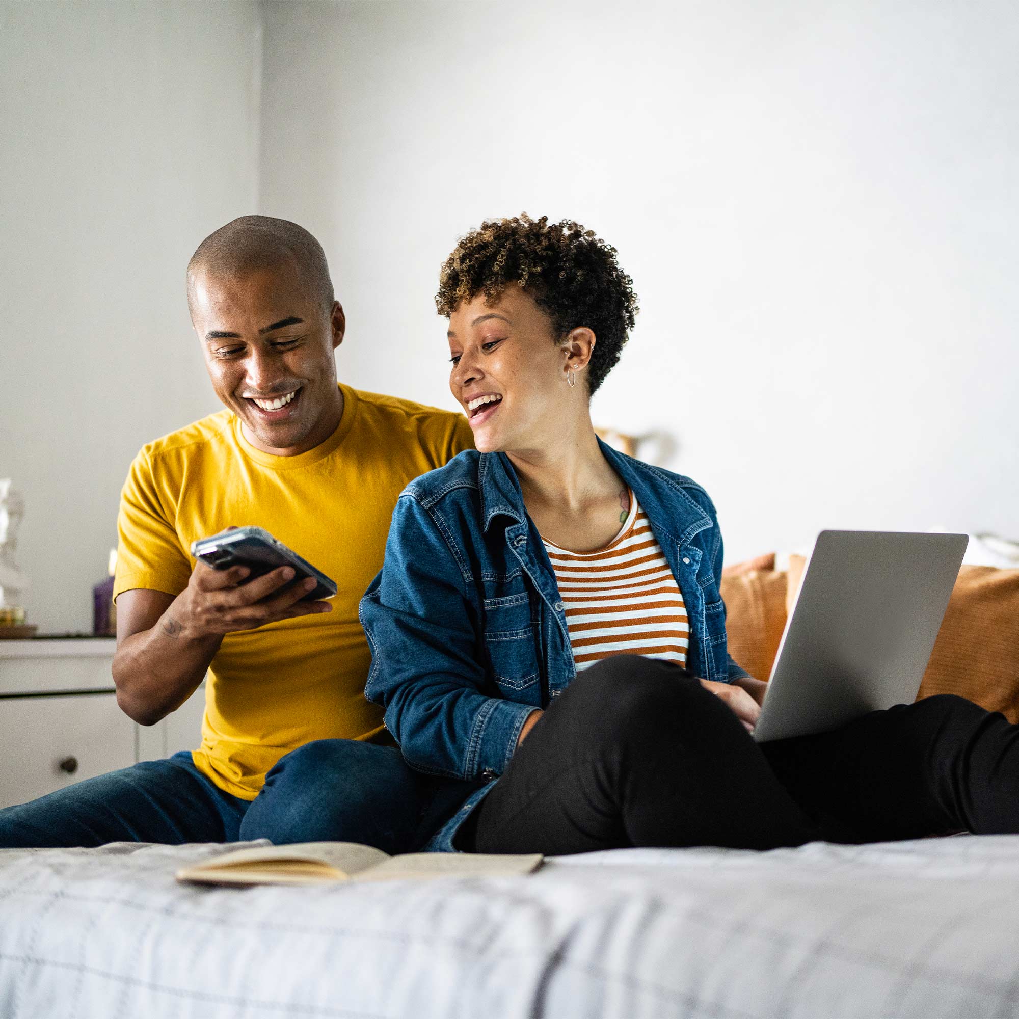 A man and a woman sitting on a bed using a computer.