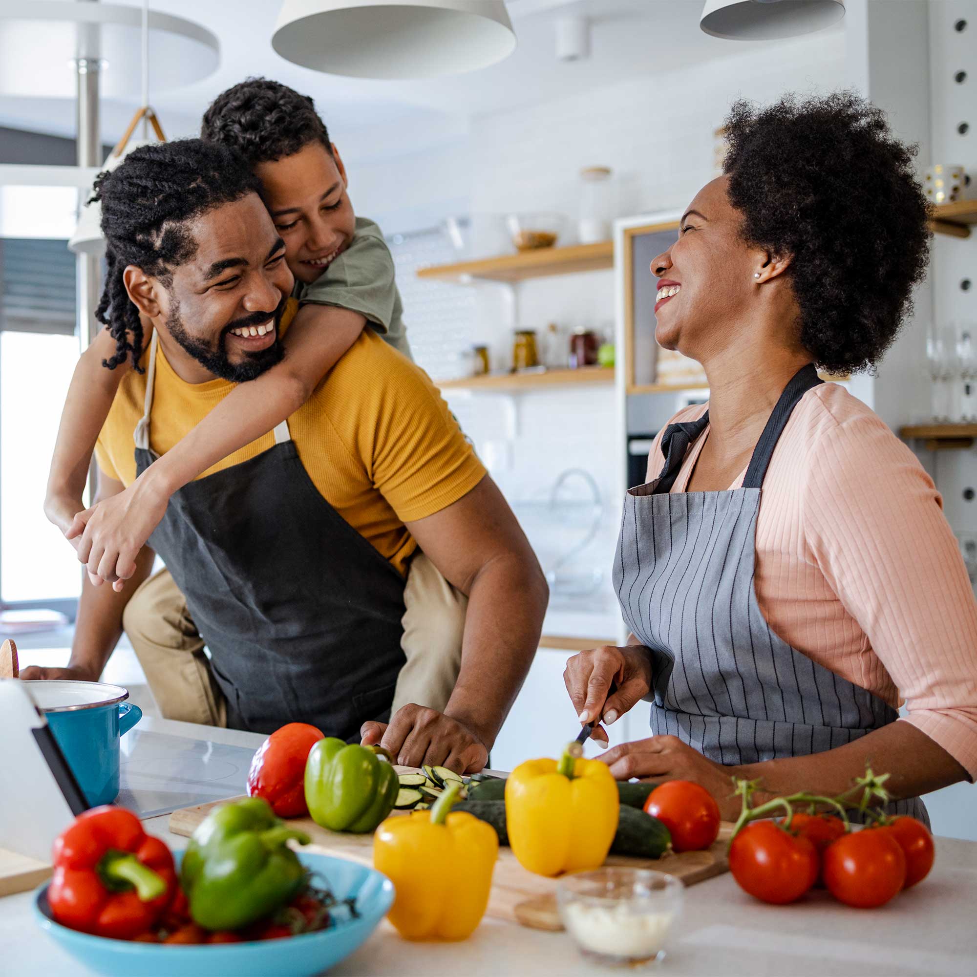 A man and woman in kitchen cooking with child on man's back laughing