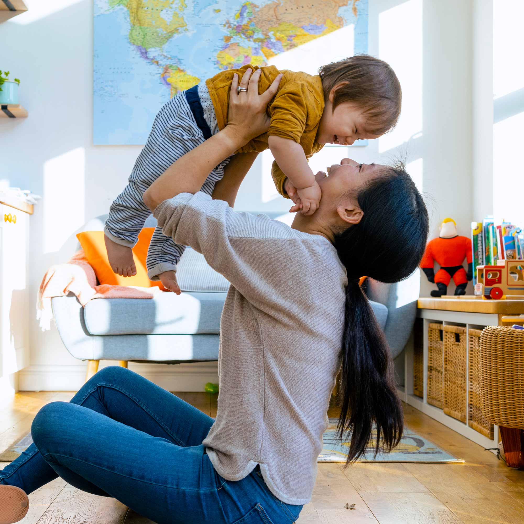 Woman sitting on the floor while holding her child in the air and smiling.