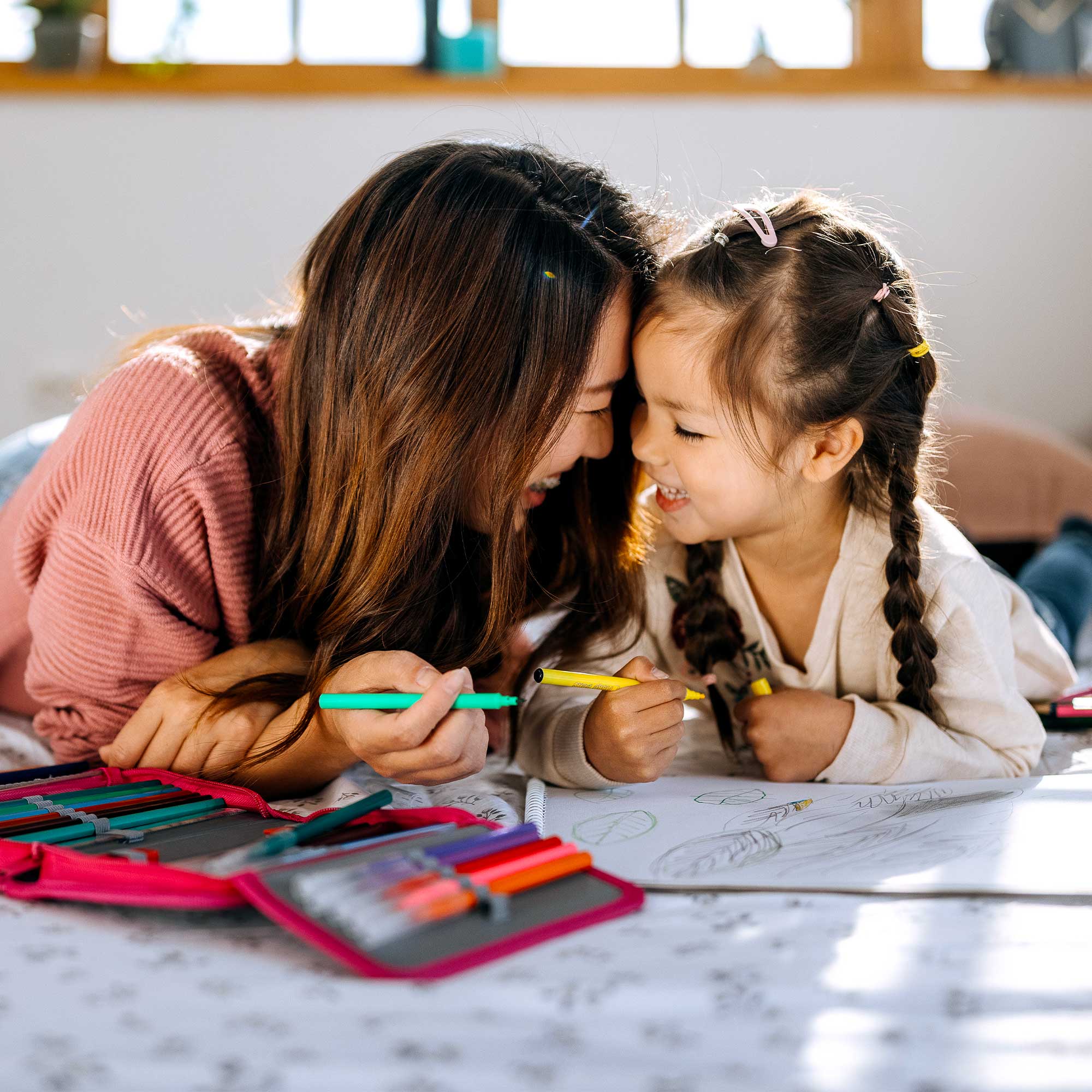A mother coloring pictures with her daughter as they lay on the floor.