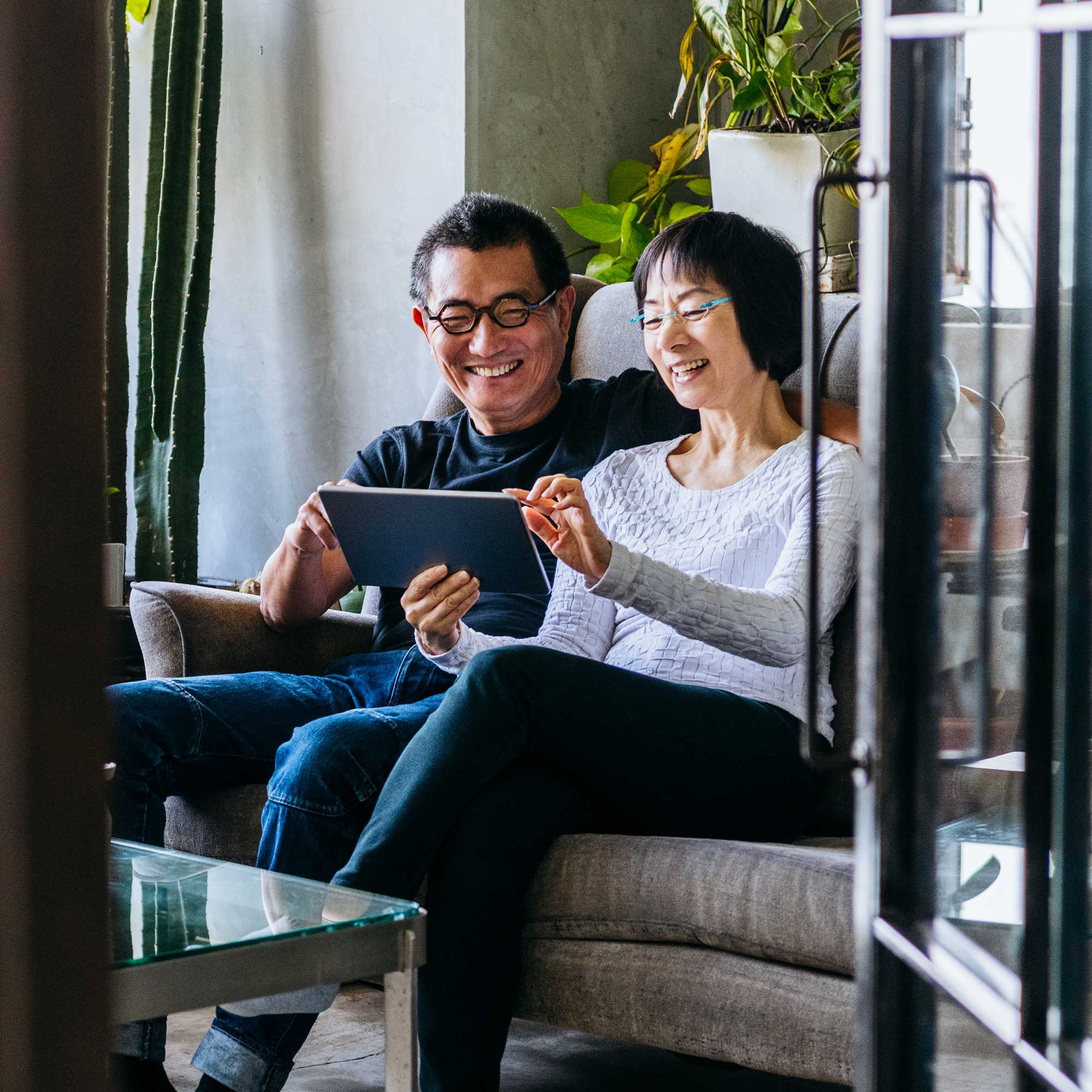 A man and woman sit on a patio chair smiling as he talks on phone.